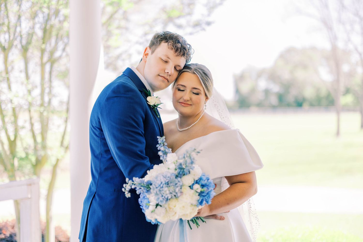 A tender moment between newlyweds captured under a white columned porch.