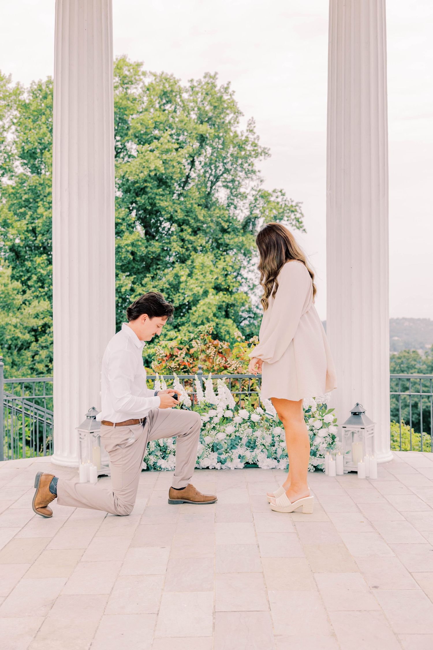 A proposal moment captured on a white columned porch with people in light colored clothing.