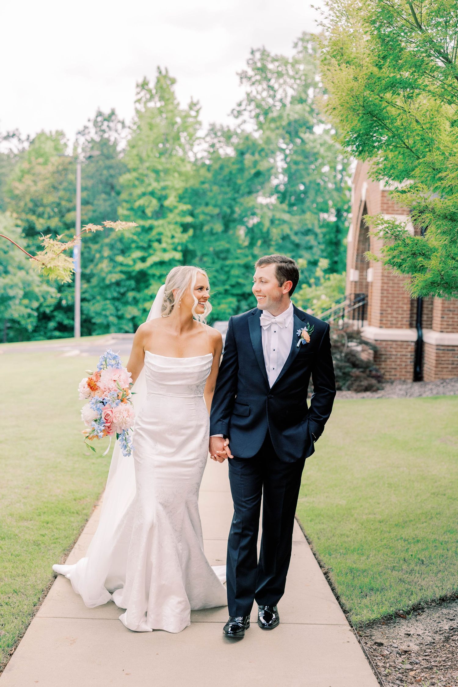 A couple walks hand in hand along a garden path on their wedding day.