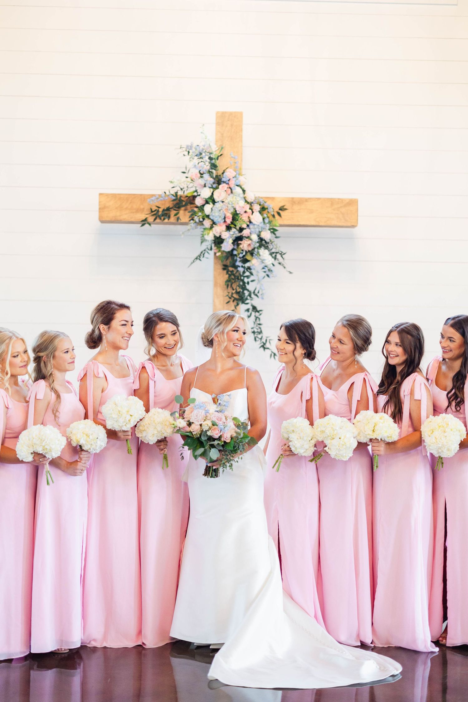 Wedding party line up showing pink bridesmaid dresses and white bridal gown against church backdrop.