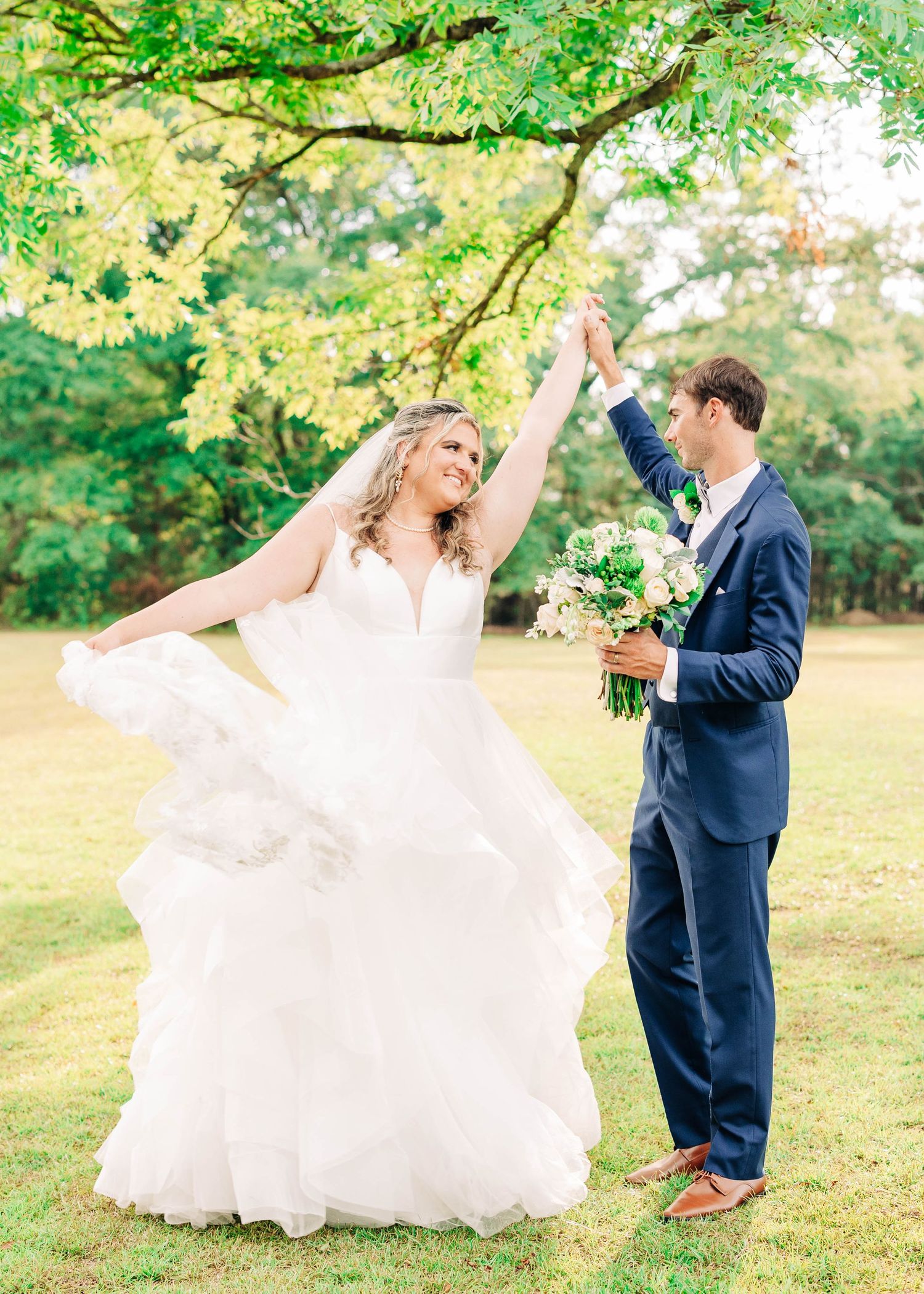 Couple dances playfully on sunlit lawn surrounded by green trees.
