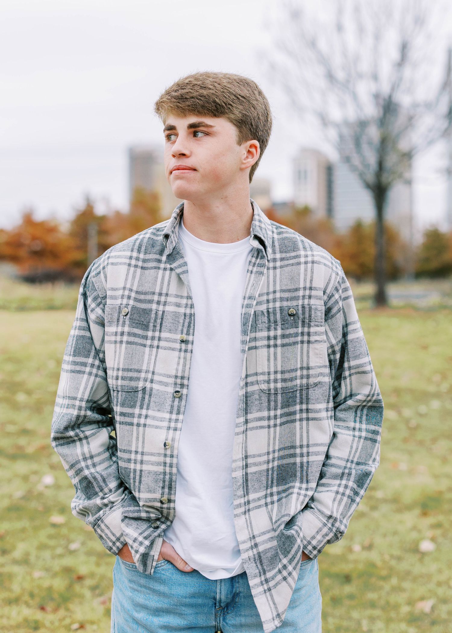 Person in plaid shirt and white t-shirt standing in autumn field setting.