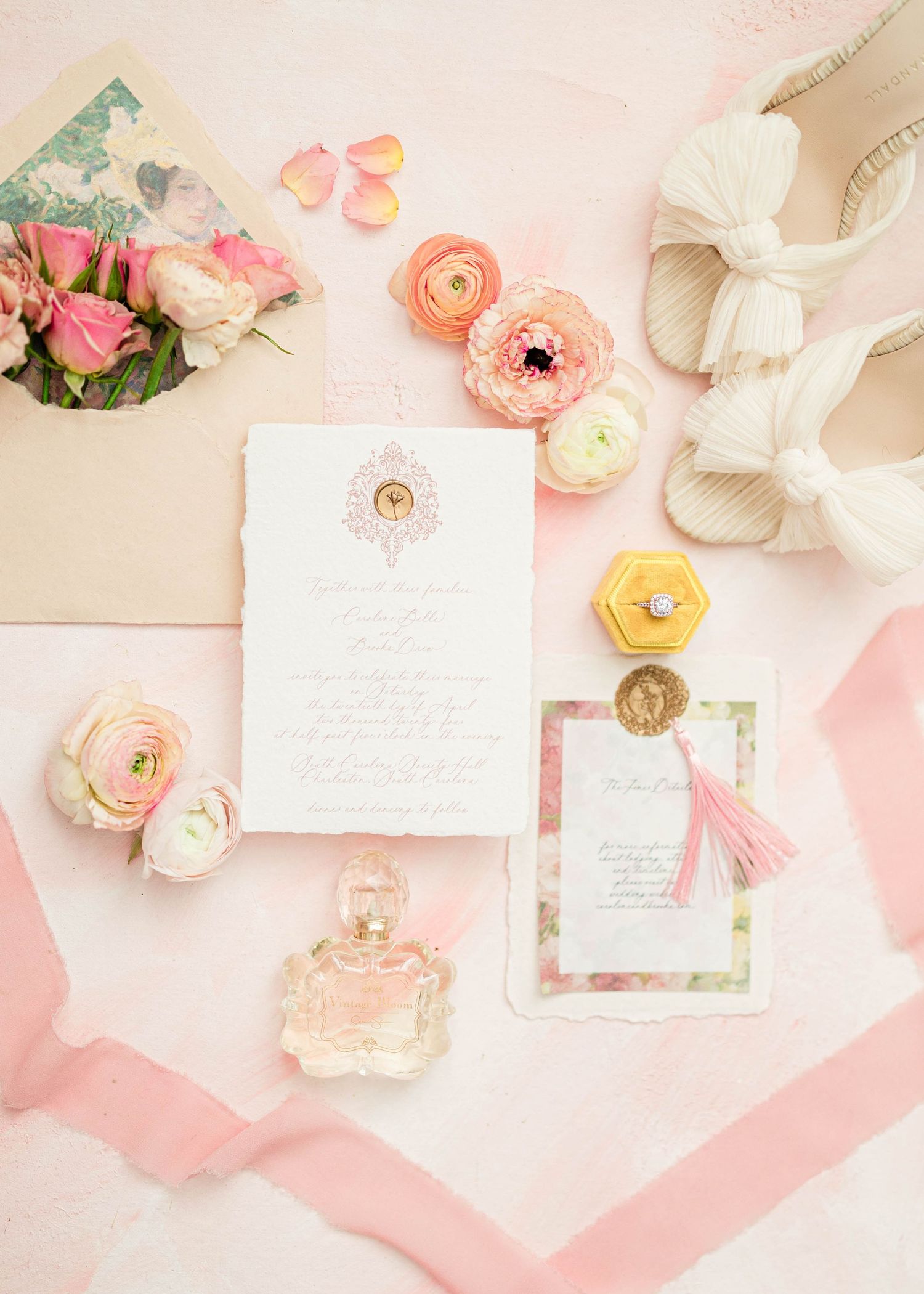 Elegant wedding invitation suite with pink flowers and perfume bottle on soft pink background.