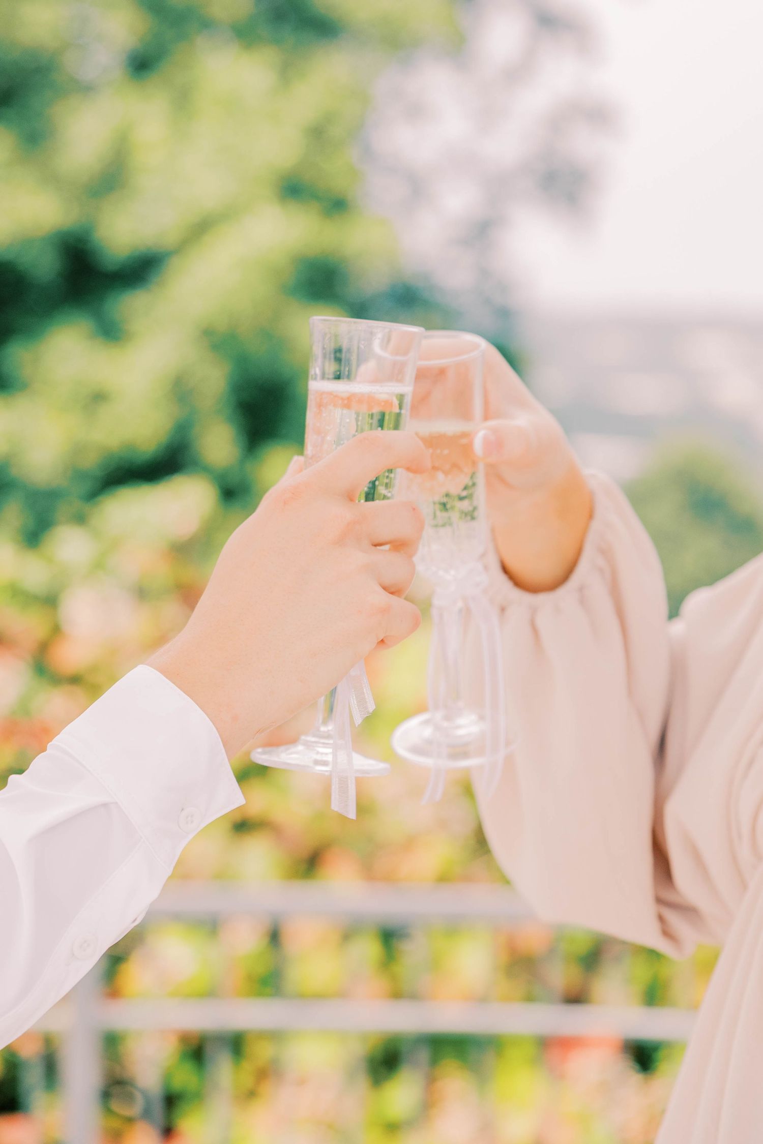 People in light colored clothing toasting with champagne glasses against a green outdoor background.
