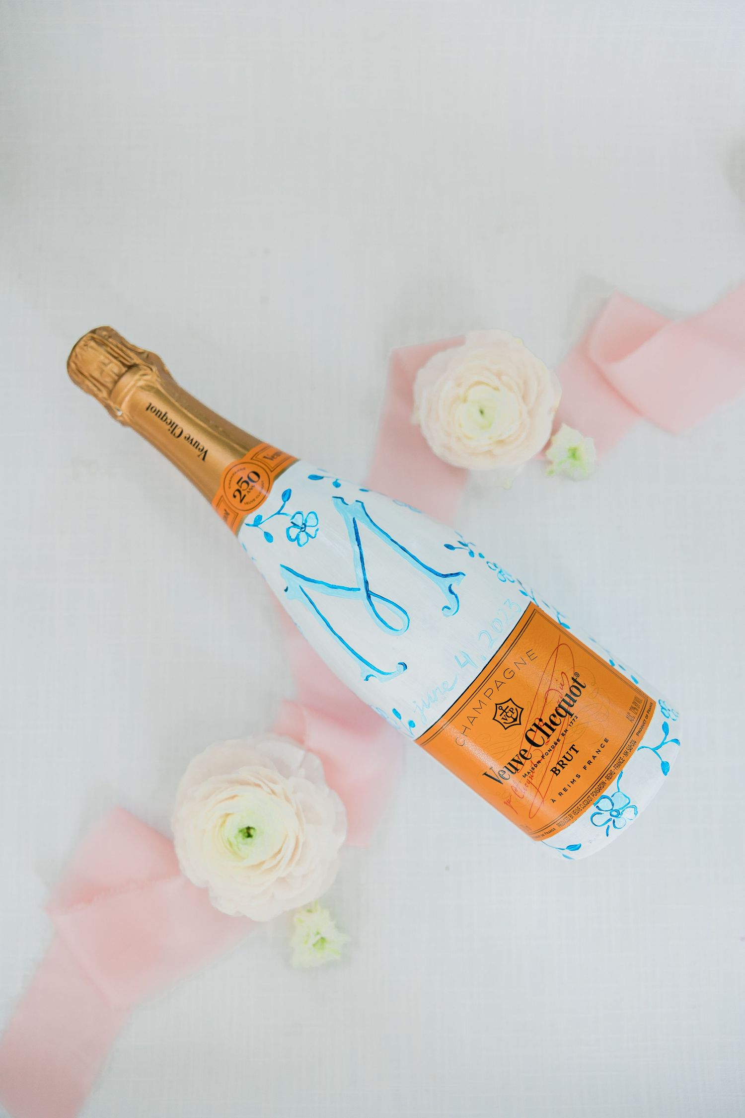 Veuve Clicquot champagne bottle with white flowers on pink background.