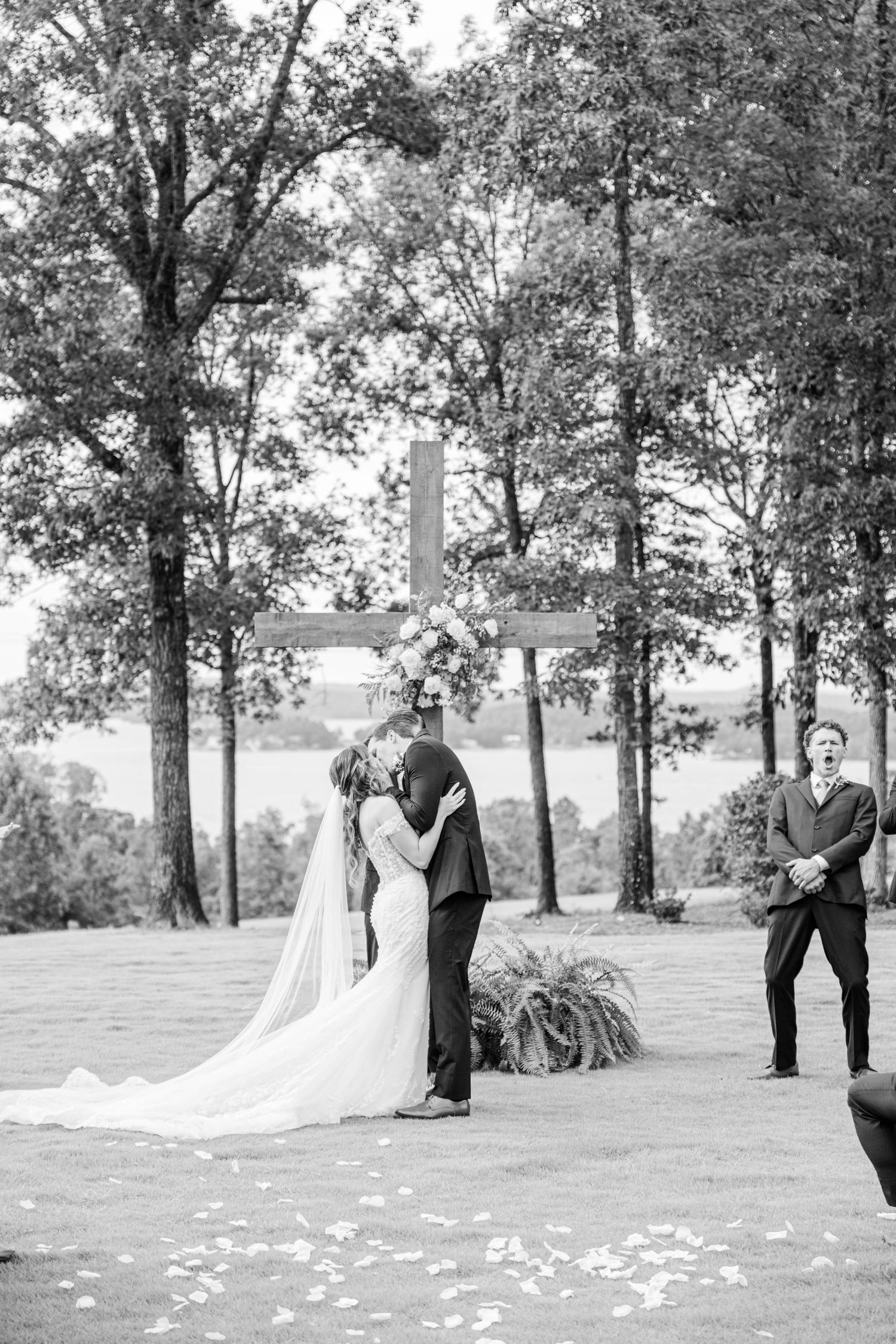 Black and white outdoor wedding ceremony with floral cross backdrop and scattered petals.