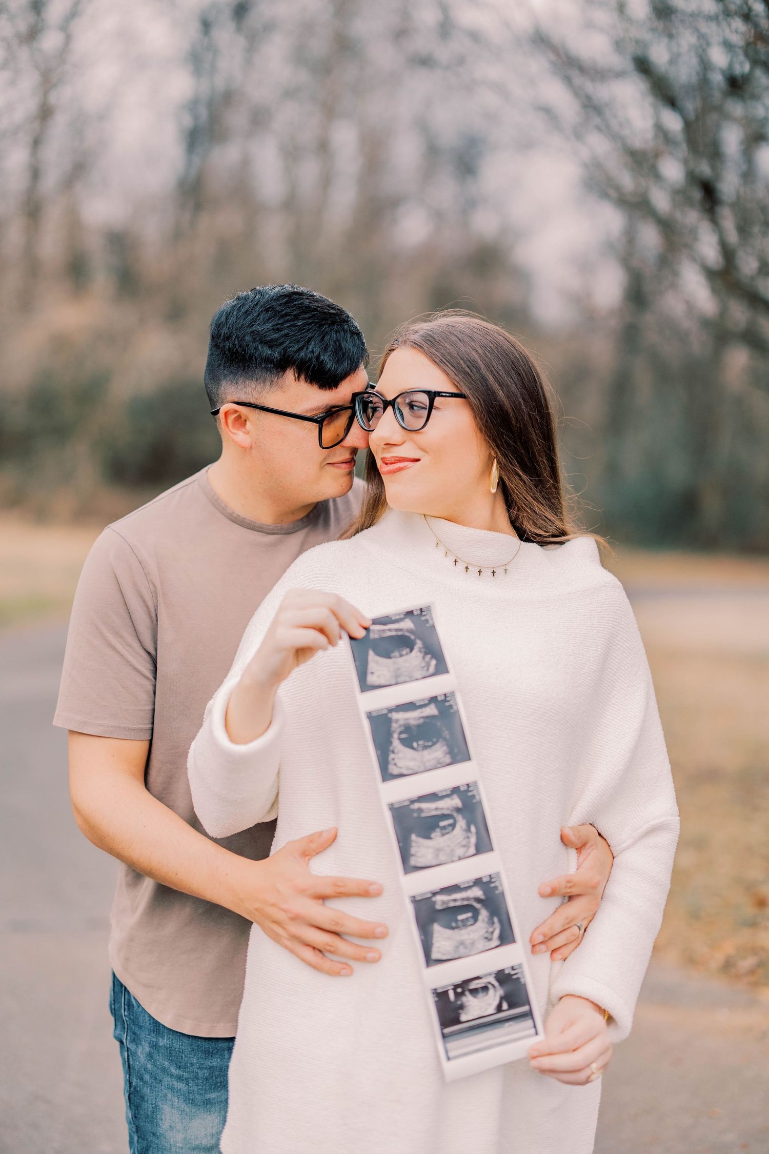 Couple holding ultrasound photos outdoors during pregnancy announcement photoshoot.