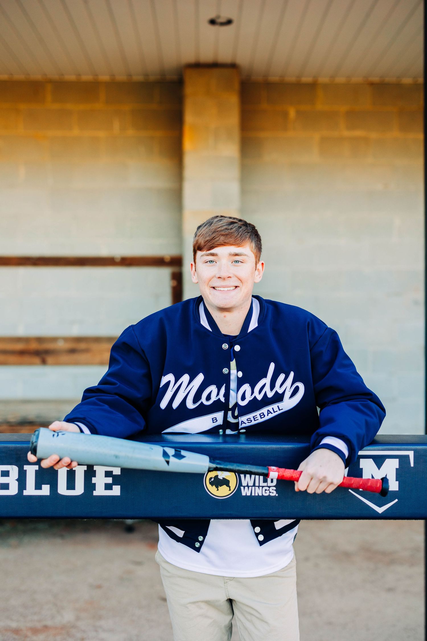 Person in blue varsity jacket holding sports banner while sitting on concrete bench.