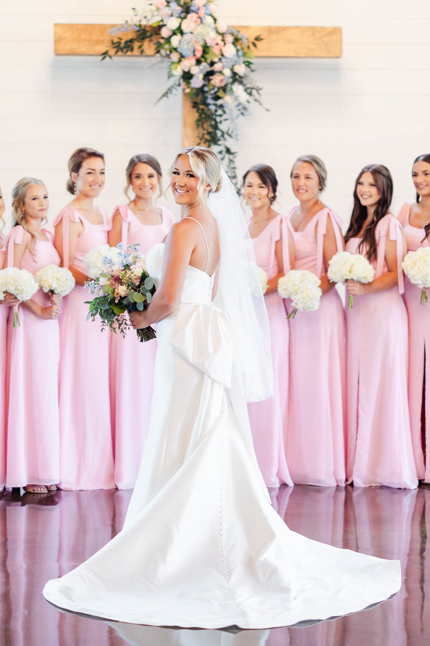 Bridesmaids in light pink dresses stand with bride in white gown inside elegant church setting.