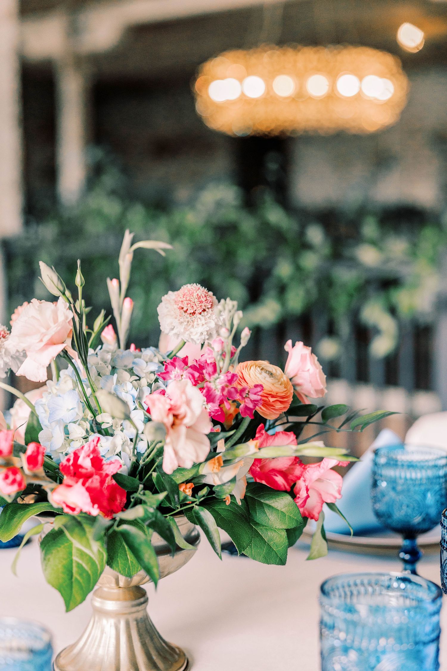 Elegant floral centerpieces with pink and coral blooms in blue vases create a romantic wedding table setting.