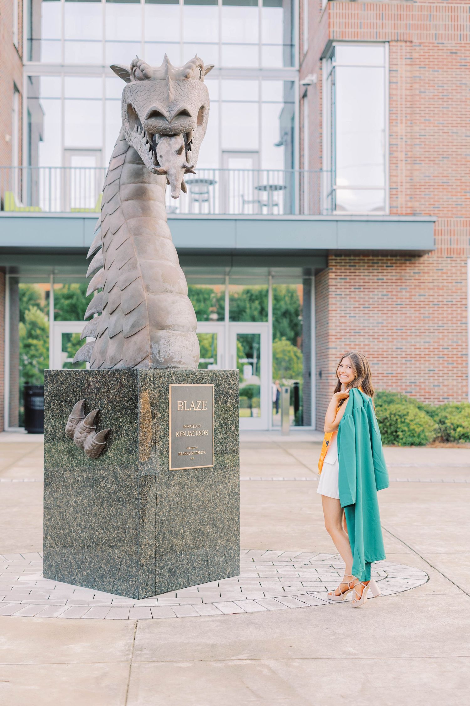 A person in a teal cardigan poses next to a large dragon statue on a university campus.
