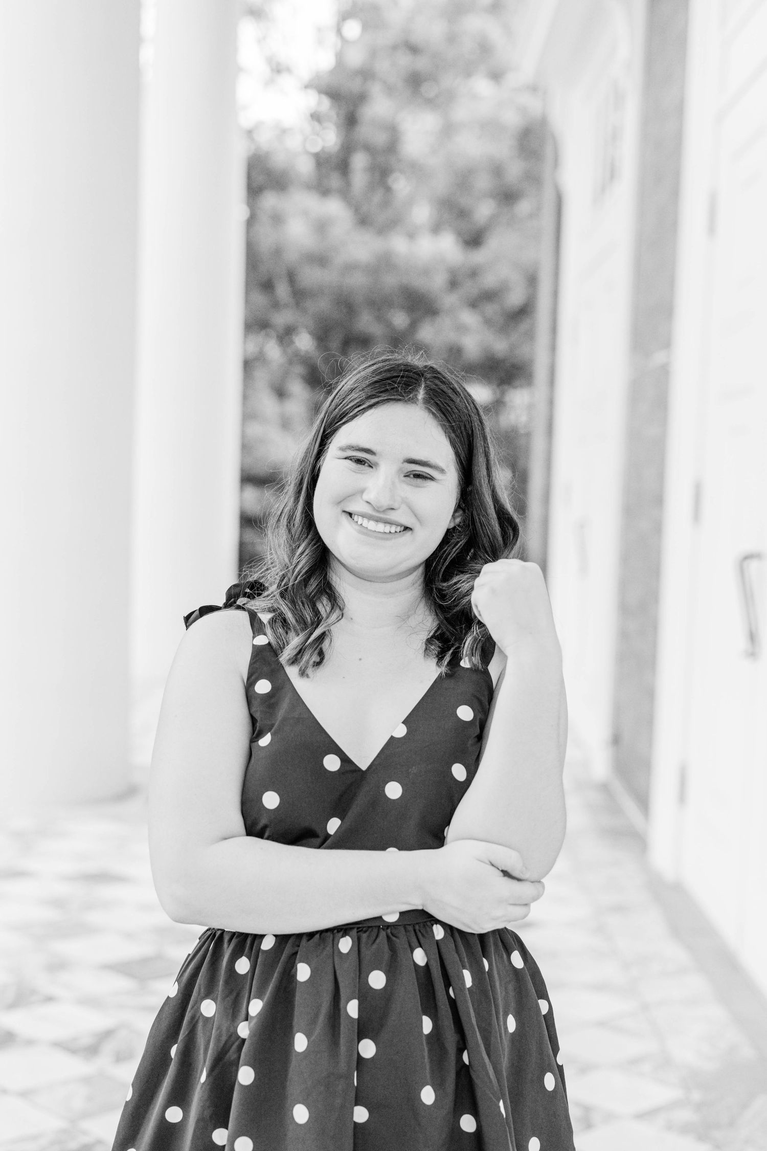 Black and white portrait of a person in a polka dot dress smiling with arms crossed.