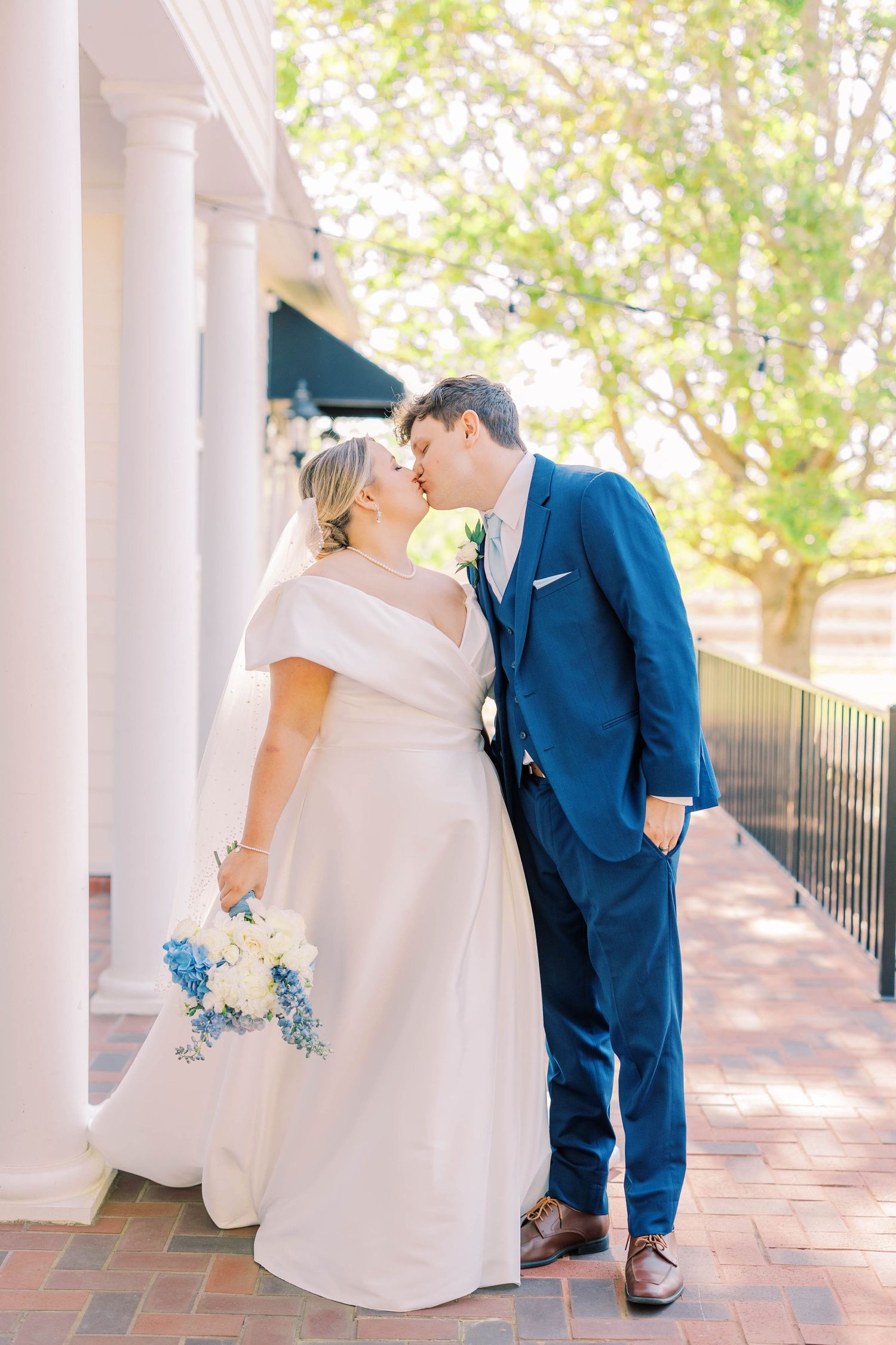 Wedding couple sharing romantic moments under white columns in outdoor setting.