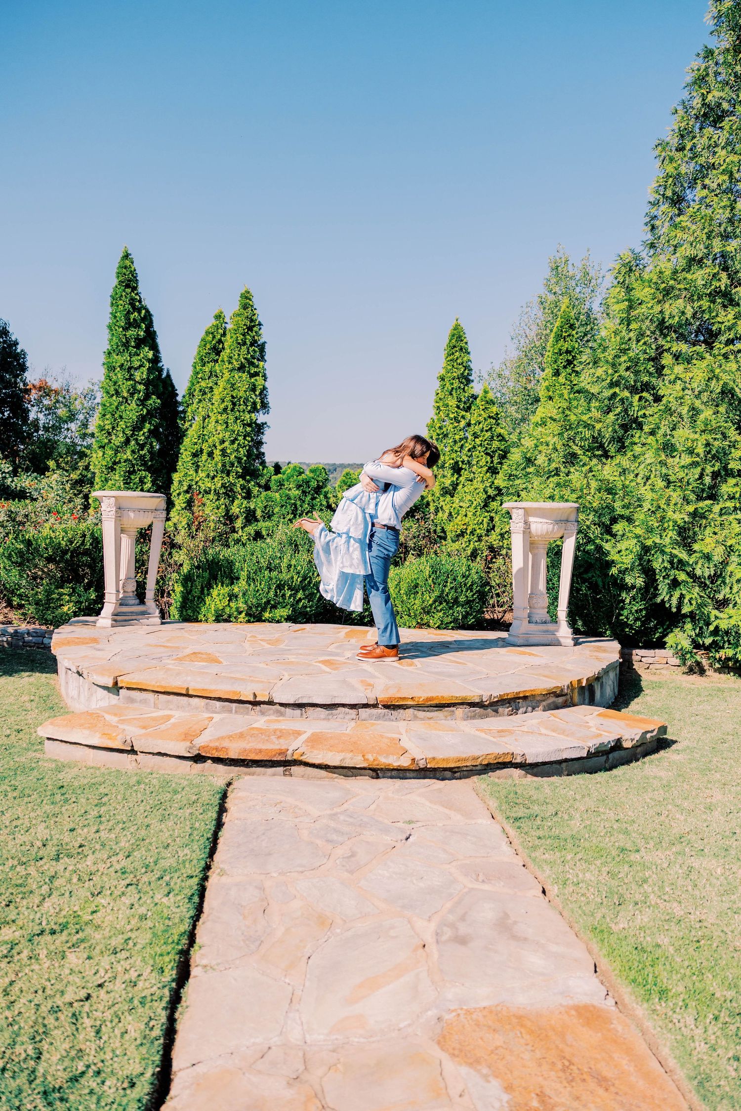 Stone pathway winding through a garden with green cypress trees.