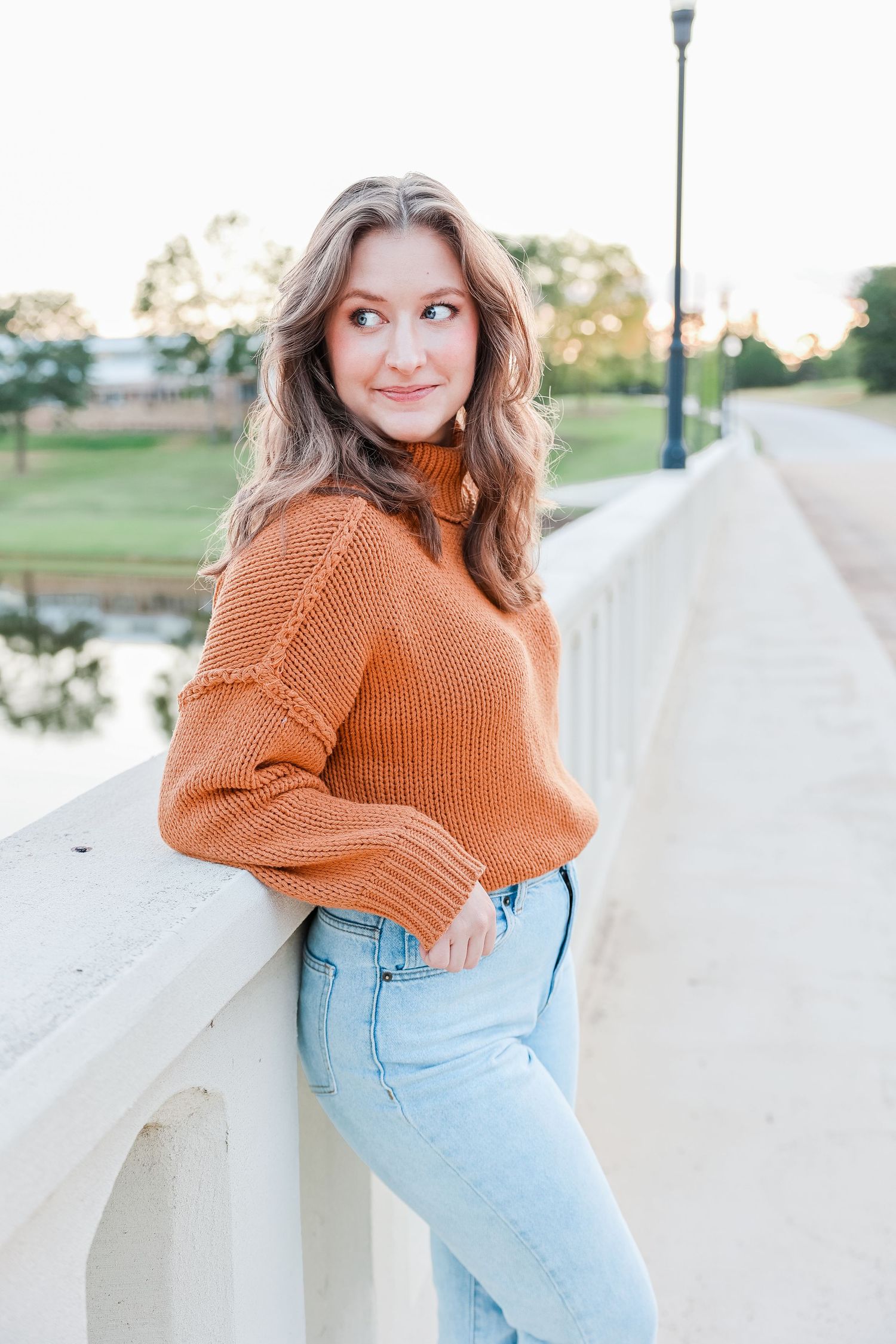 Casual portrait series wearing orange sweater and jeans while leaning on white railing.