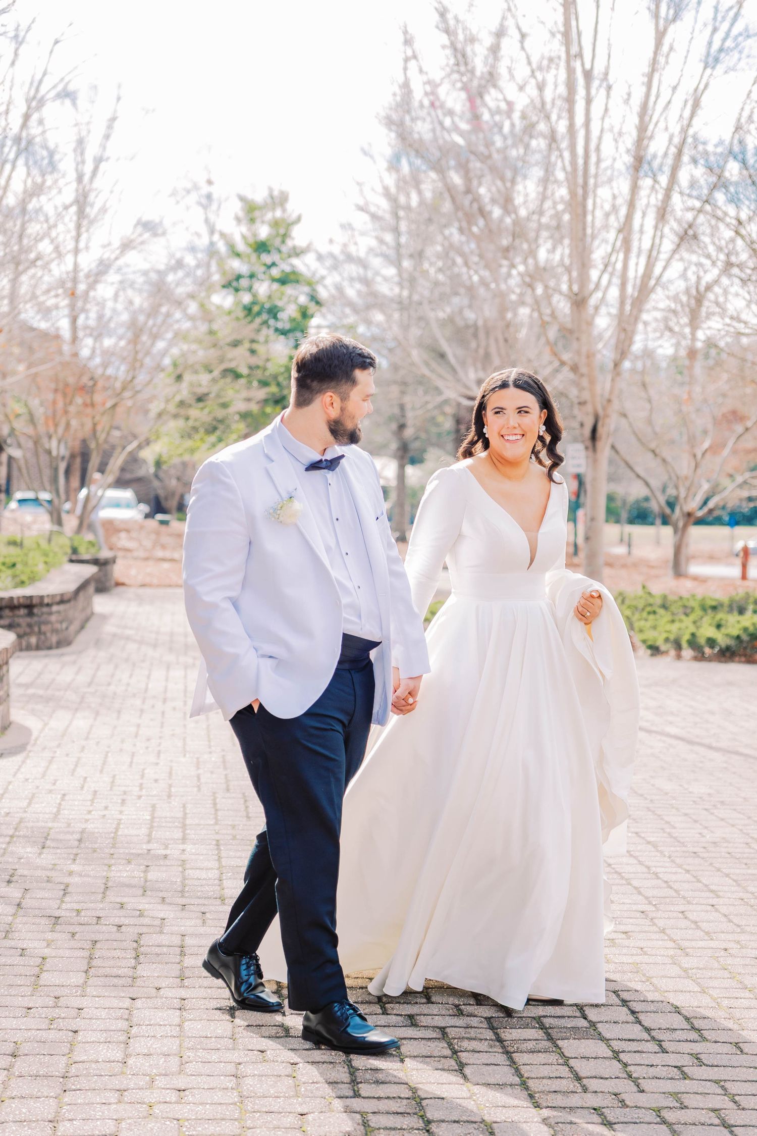 A romantic outdoor wedding portrait of a couple walking on brick pavement in formal attire.