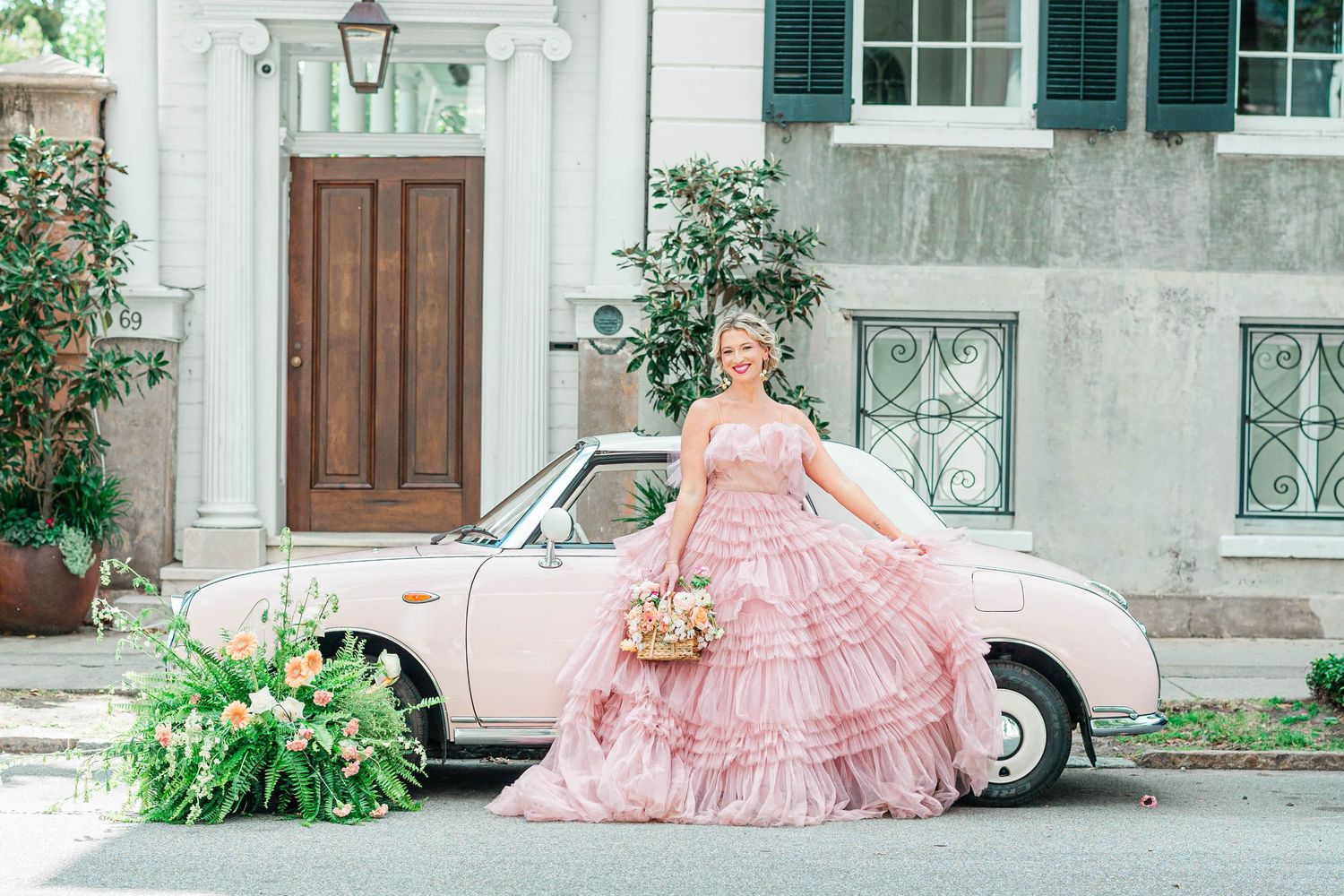 A dreamy portrait with a pink ruffled gown against a vintage pink car and historic building.