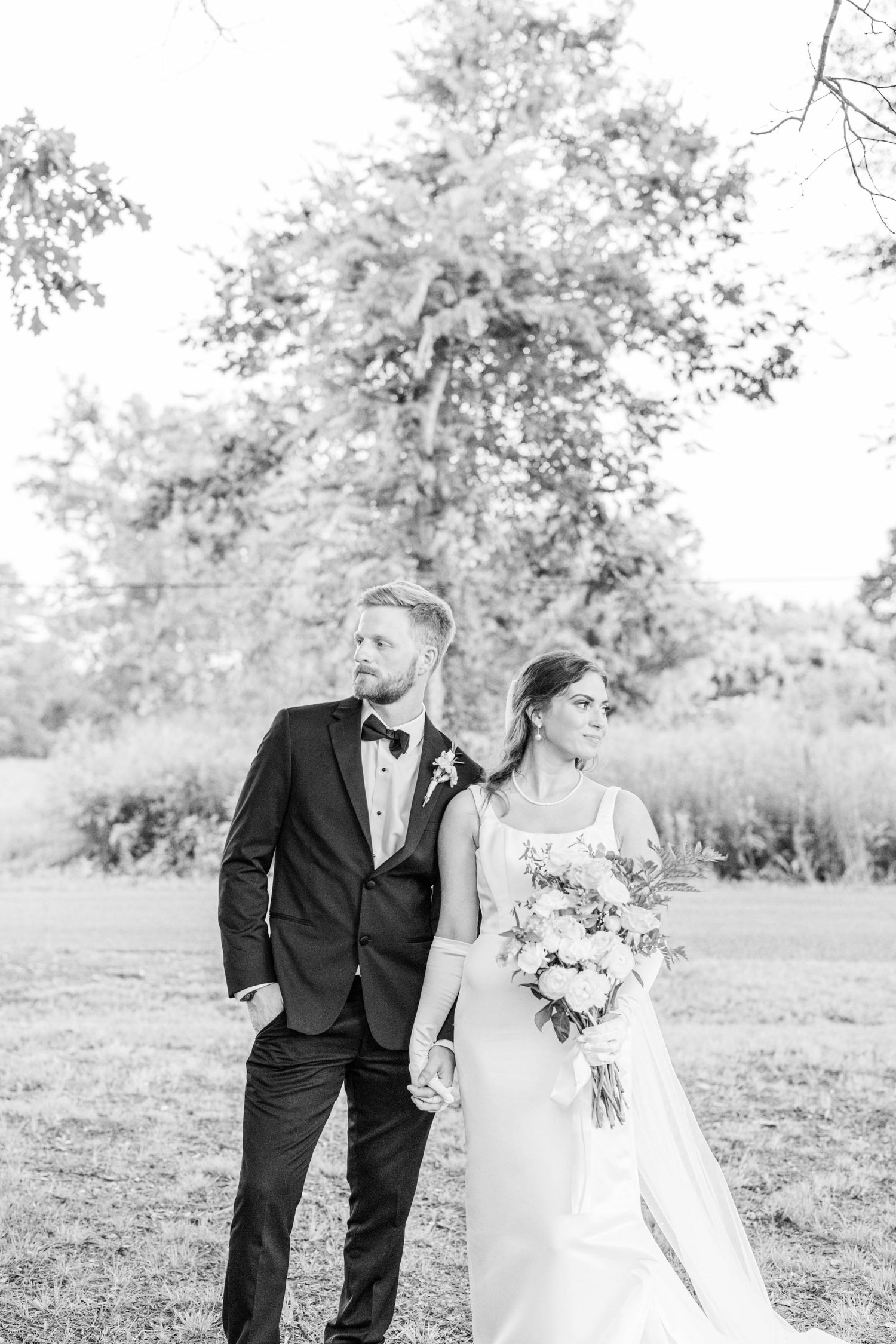 A black and white wedding photo of a couple posing outdoors with the bride holding a bouquet.