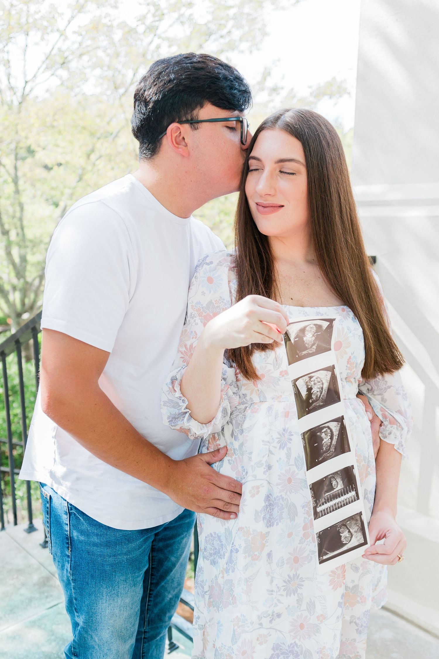 A couple sharing a tender moment while holding ultrasound photos during a pregnancy announcement.