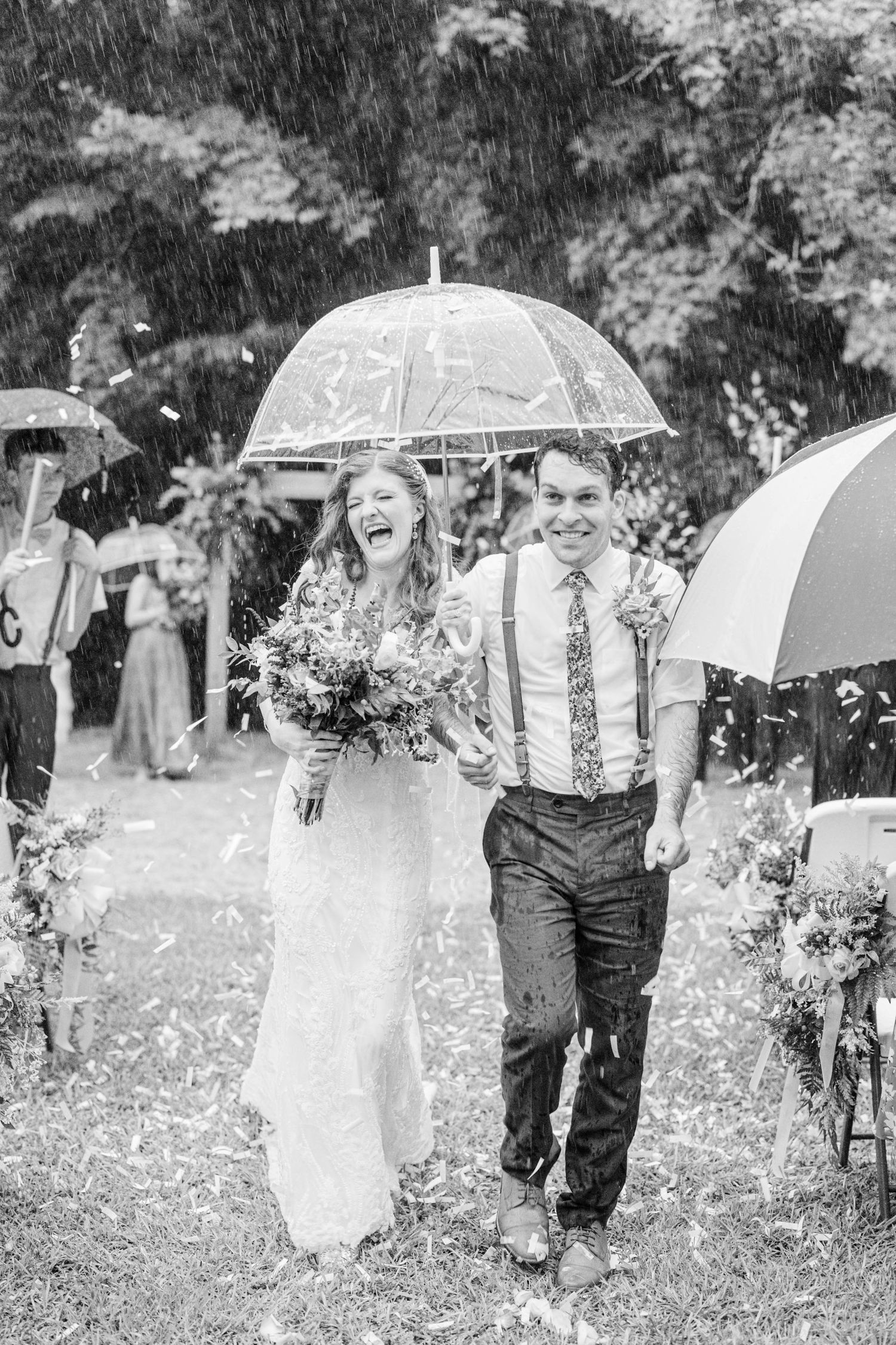 Wedding party walking through rain with umbrellas in black and white photography.