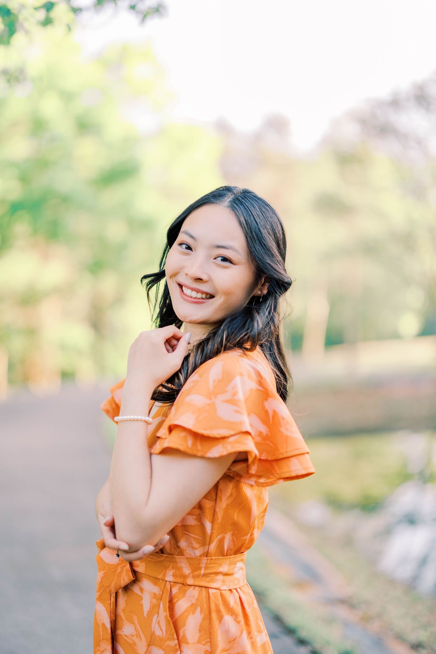 A person in an orange ruffled dress poses playfully outdoors.