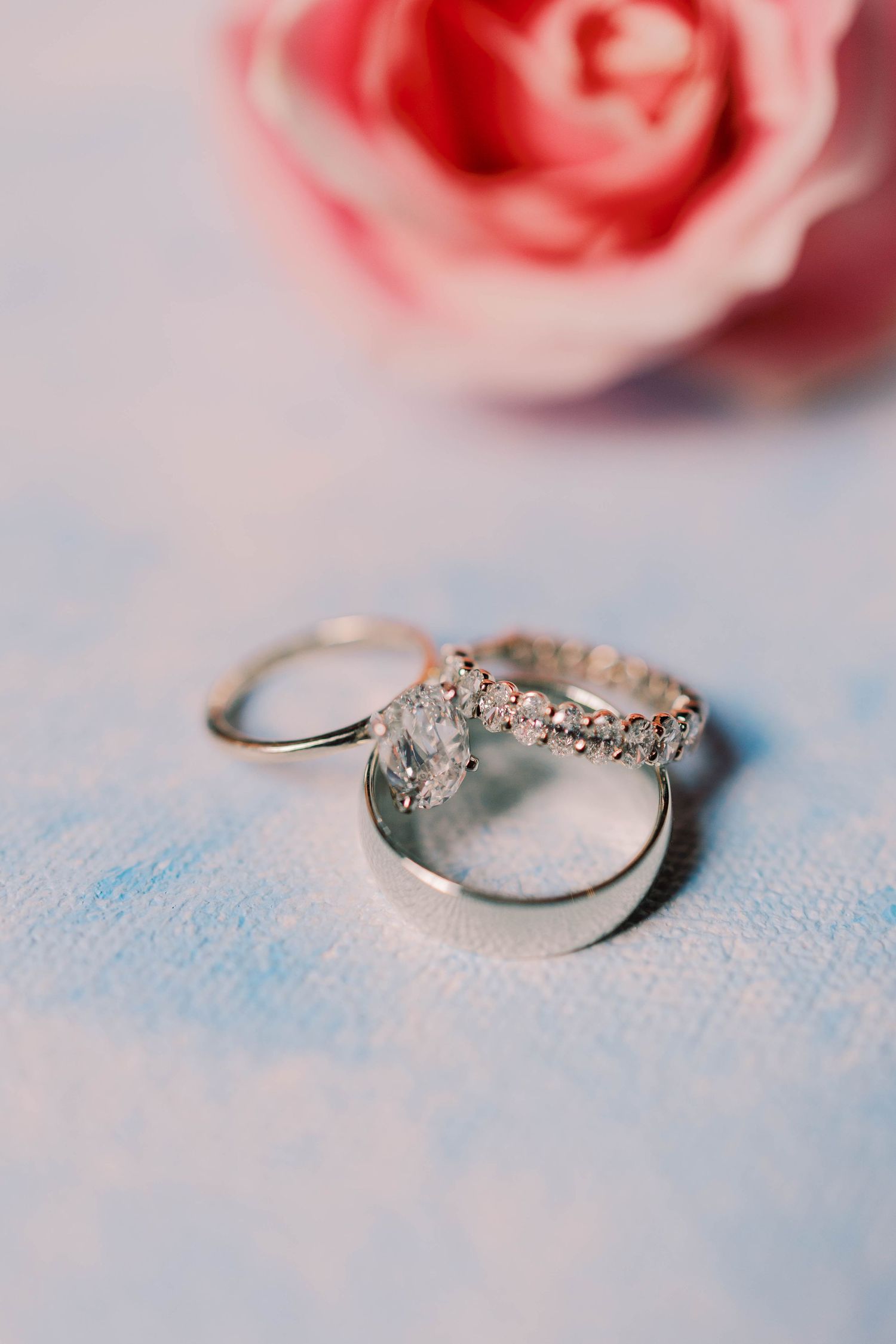 Silver engagement ring with sparkling diamonds photographed in sequence against soft pink roses and blue background.
