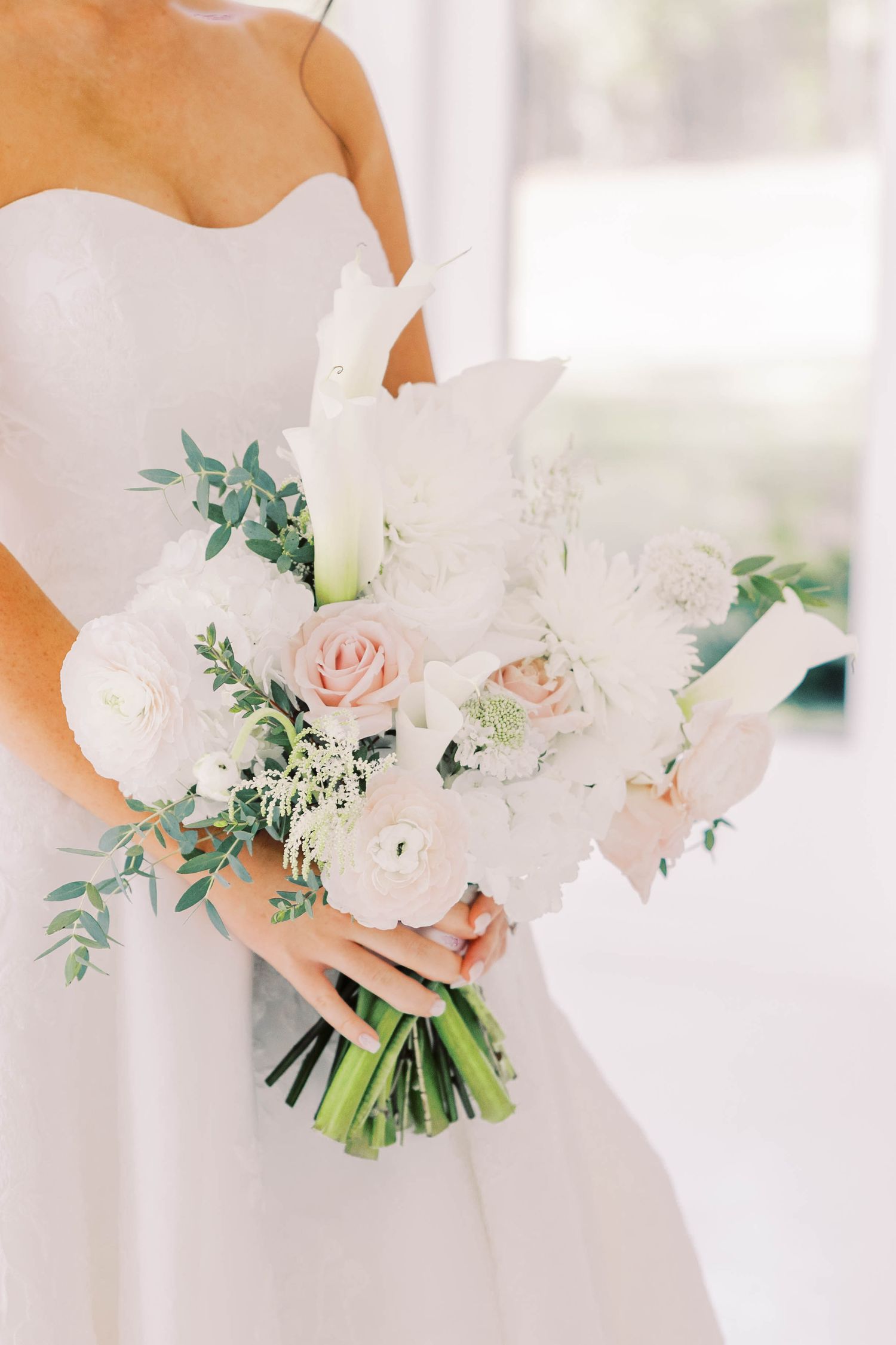 Elegant white bridal bouquet with roses and greenery against light background.
