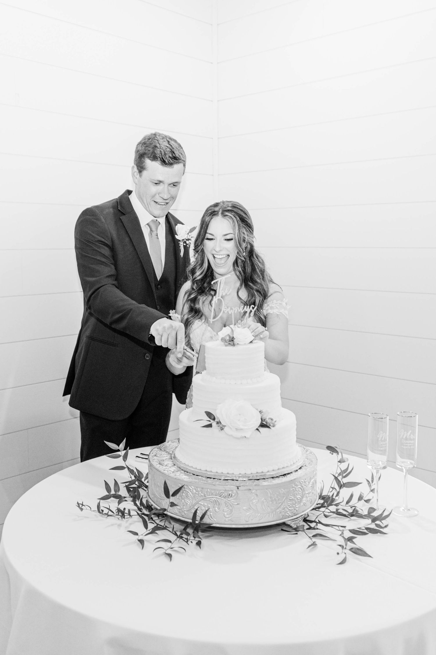 Black and white photo of newlyweds cutting their elegant three-tiered wedding cake.