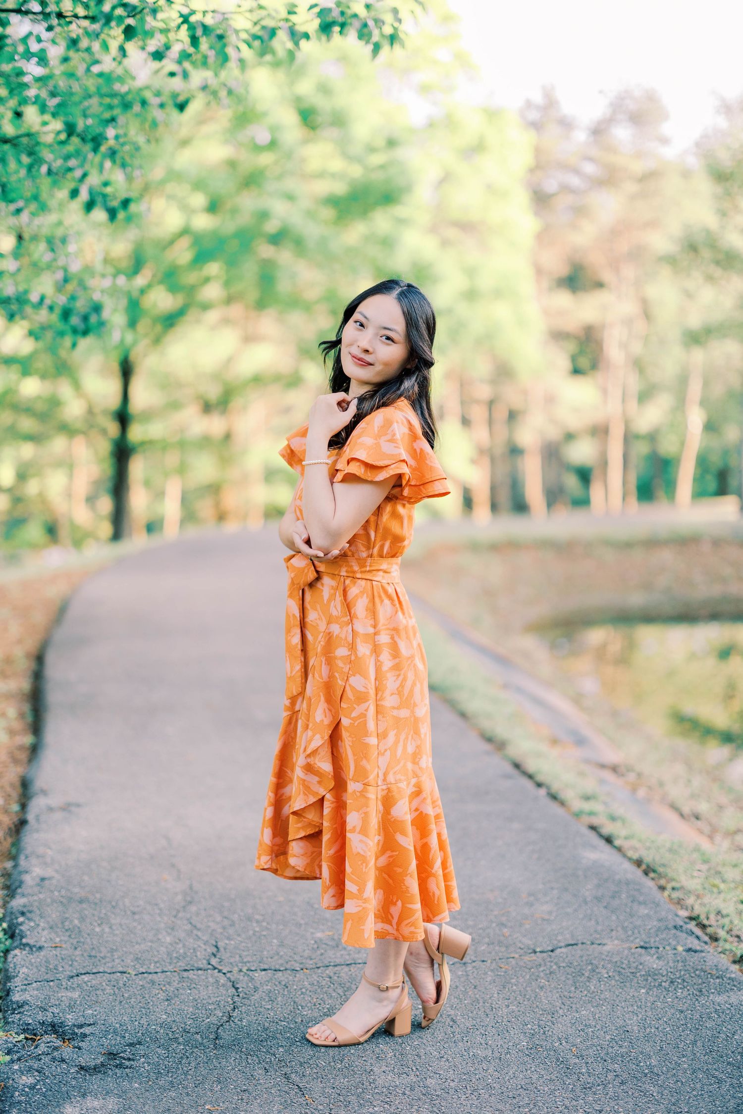 Someone twirls in an orange dress on a paved path surrounded by trees.
