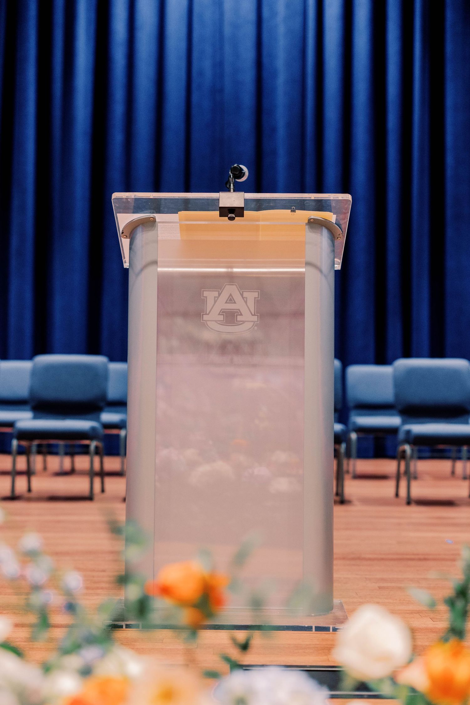 Clear podiums arranged in front of a deep blue curtain with orange floral decorations.