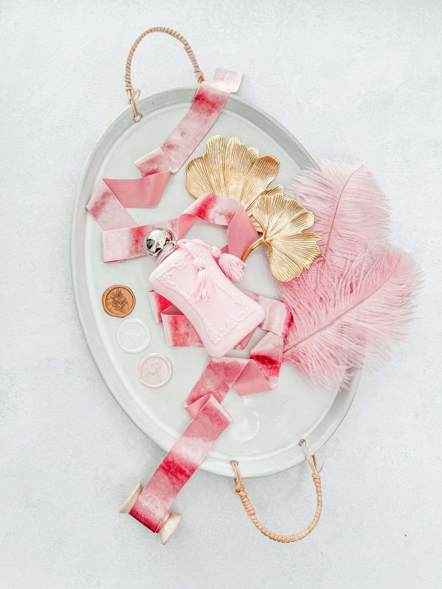 Pink and gold styled flat lay with ribbons, feathers and decorative elements on oval tray.