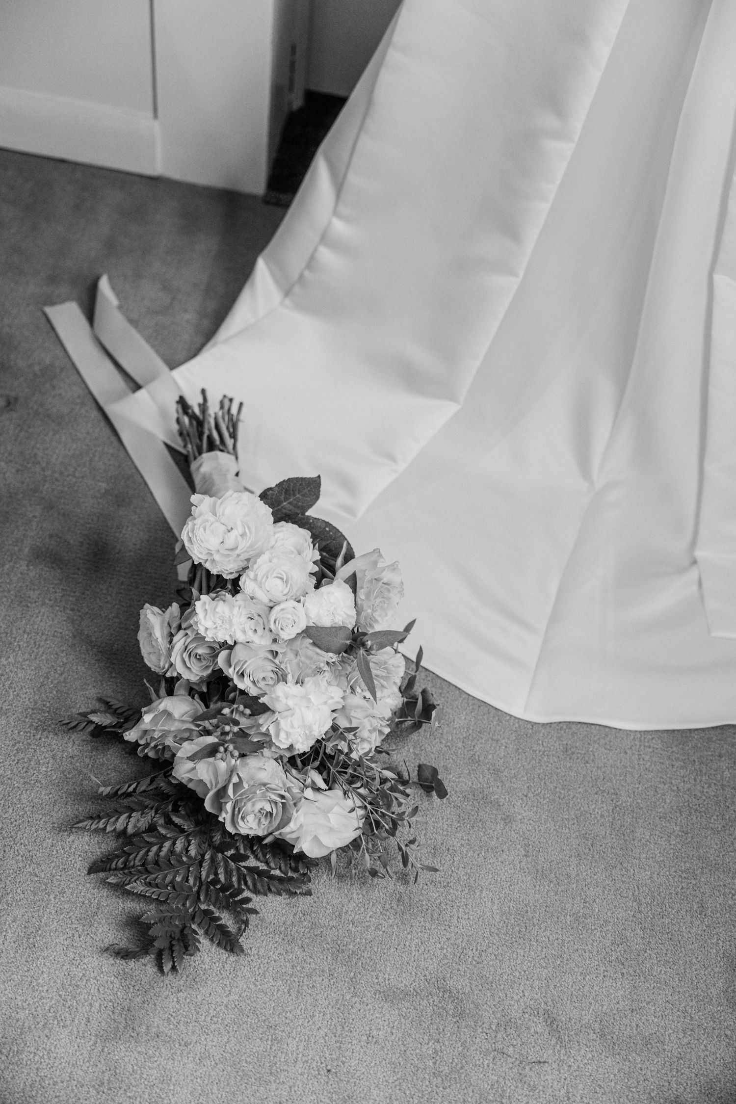 Black and white photo of a bridal bouquet with white flowers and ferns on carpet.