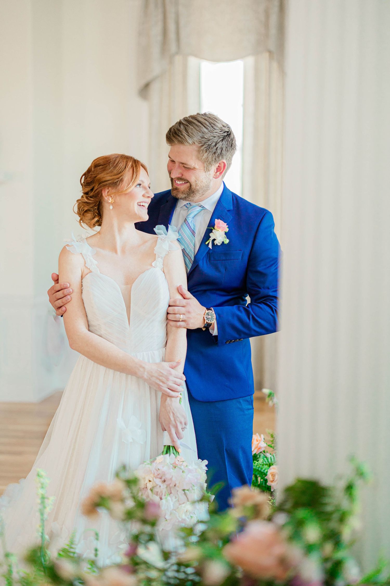 A joyful wedding couple sharing a romantic moment, with the groom in bright blue suit and bride in white gown.