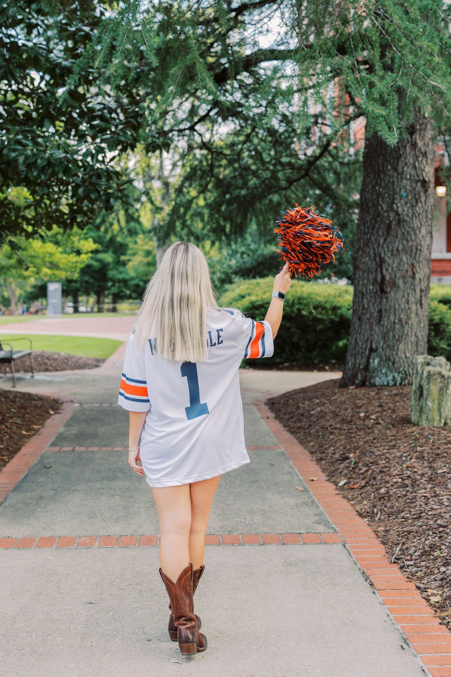 Person wearing white sports jersey with number 1 walking on brick path through garden setting.