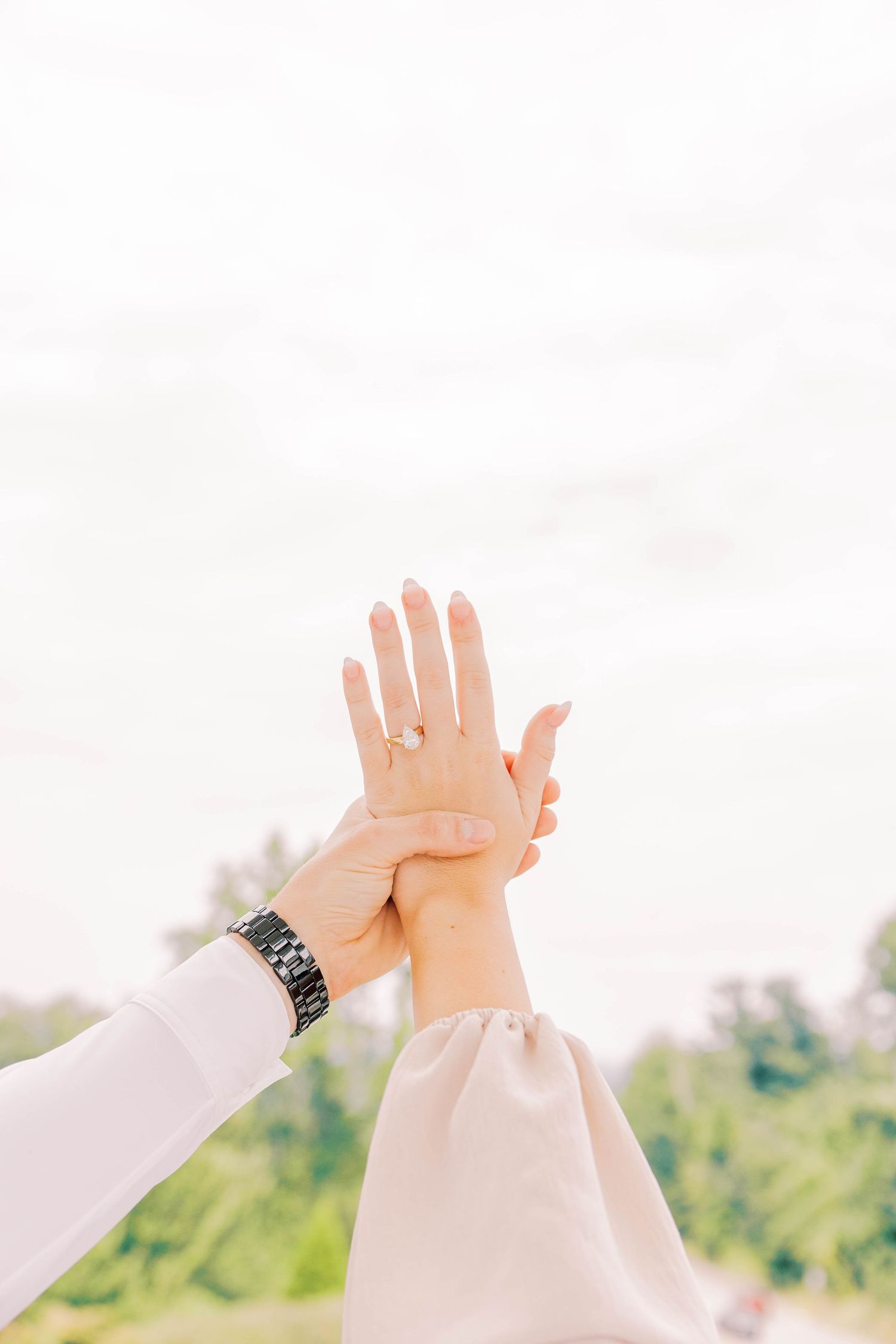 Hands raised against bright sky showing engagement ring.