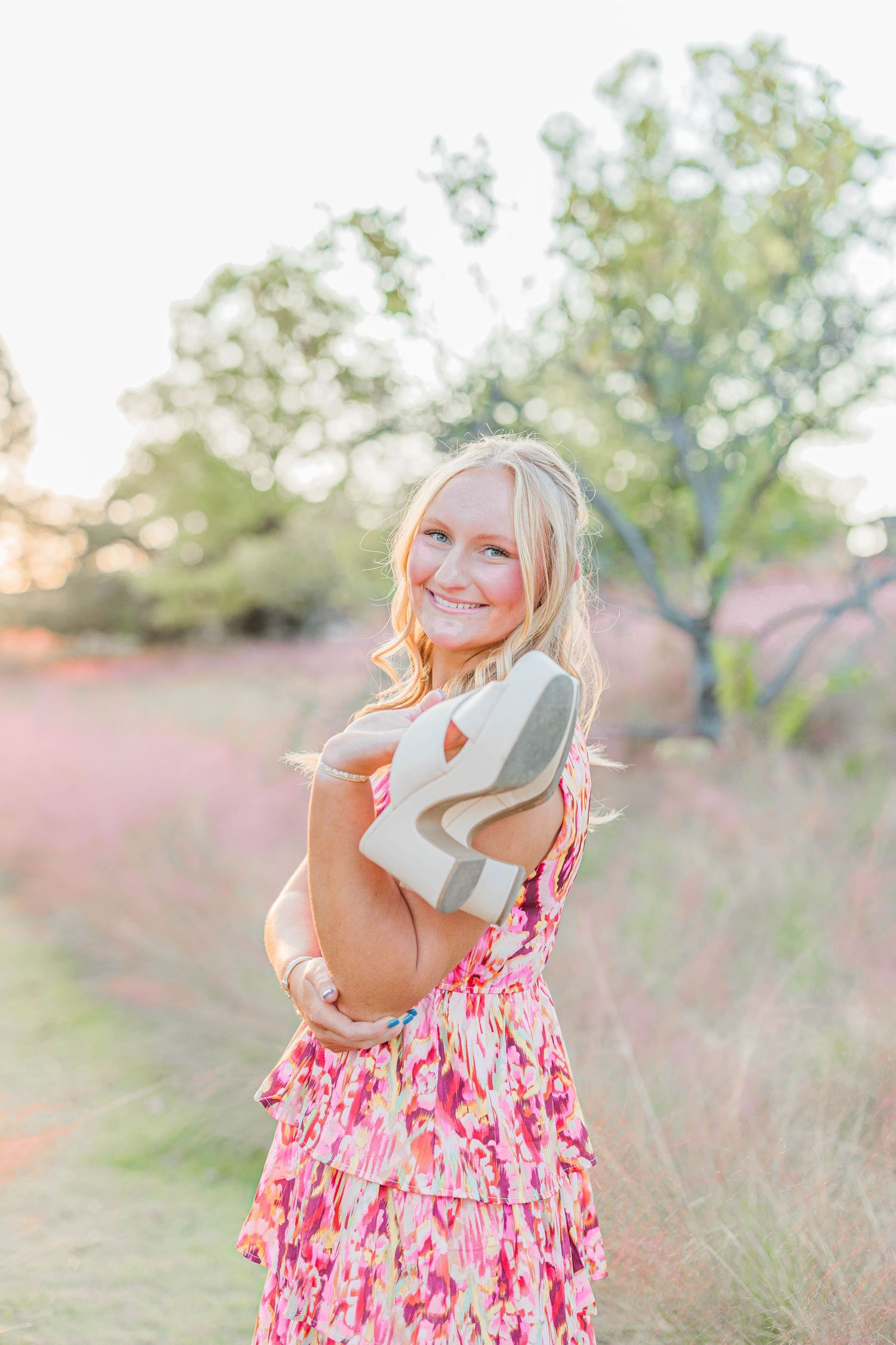 Person in pink floral dress twirling in golden sunset field.