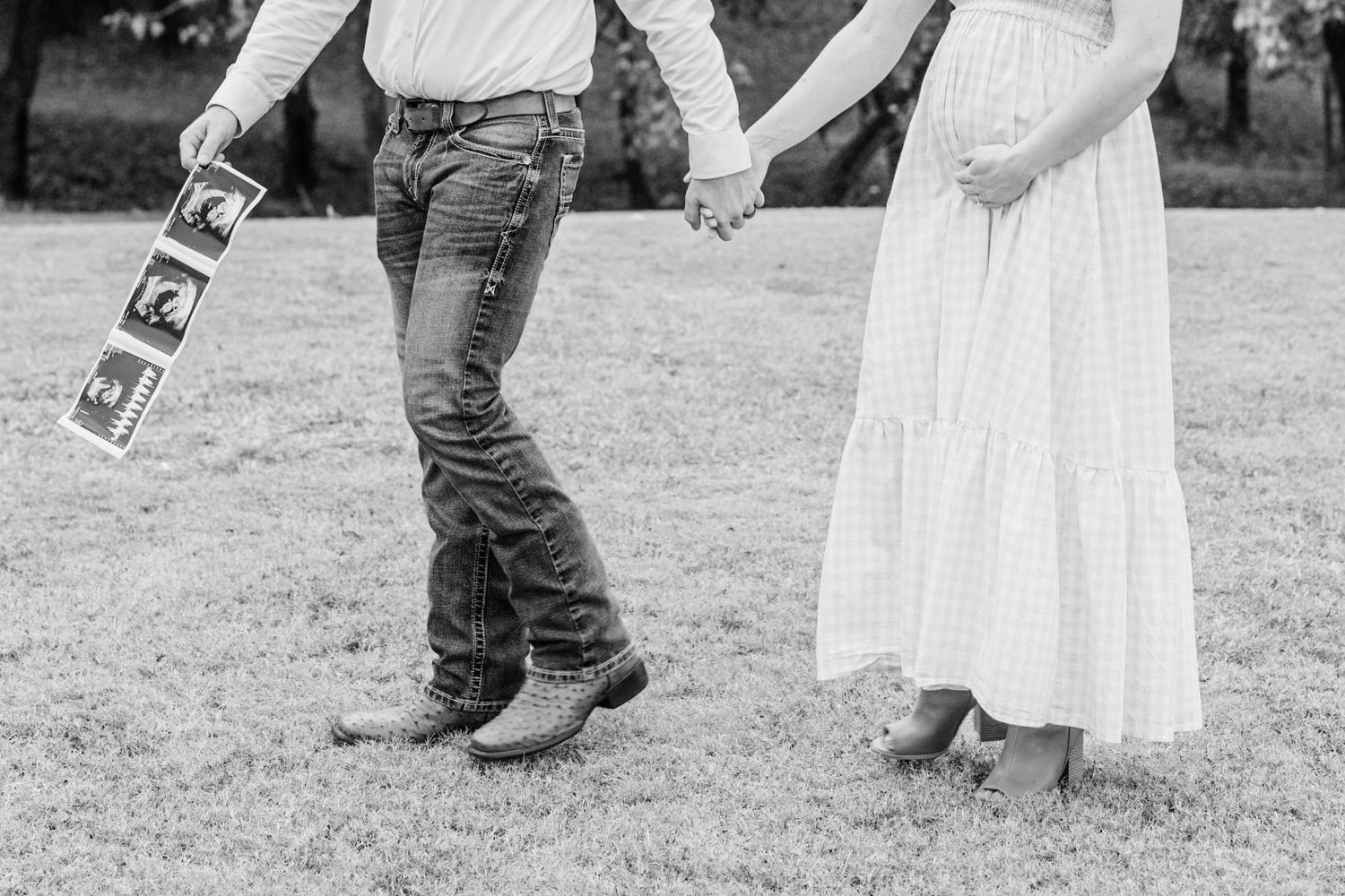 A couple shares a romantic moment outdoors while holding ultrasound photos.