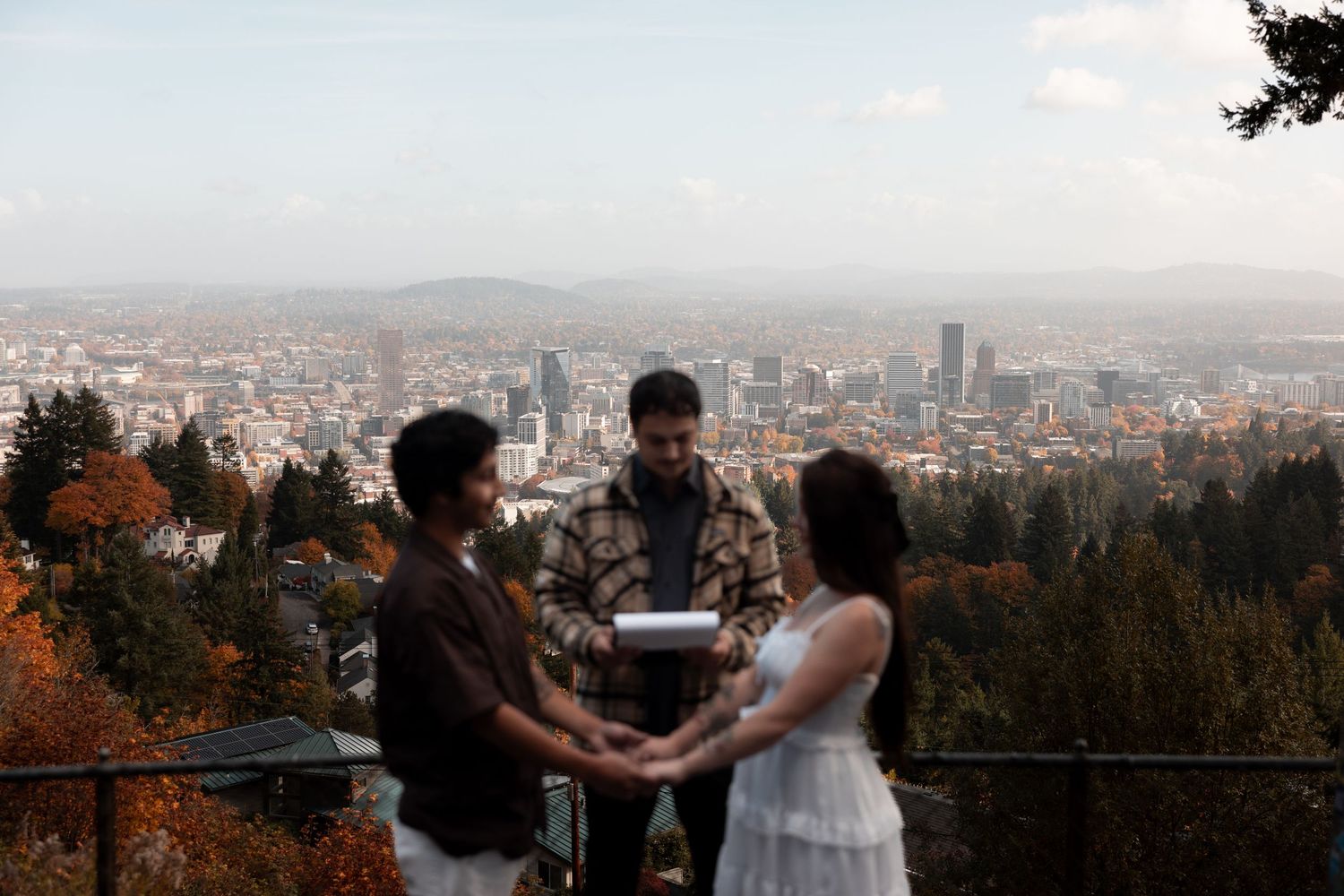 A couple shares a romantic moment at a scenic overlook with a sprawling cityscape view in the background.