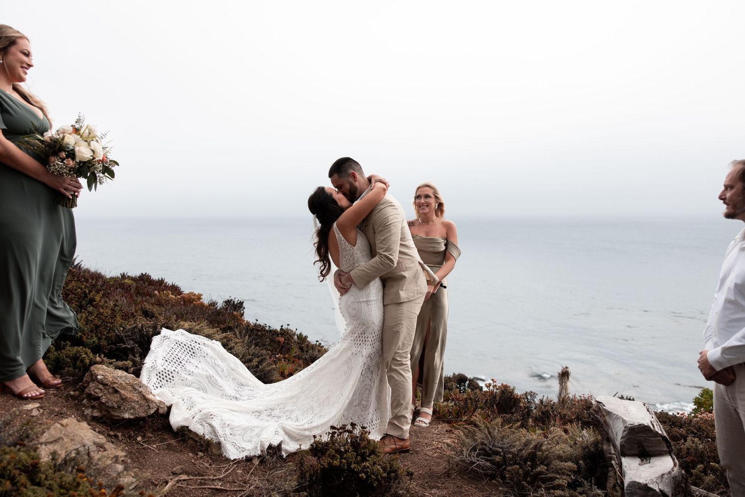 A couple shares a romantic moment on a scenic coastal cliff overlooking the ocean during their wedding photoshoot.