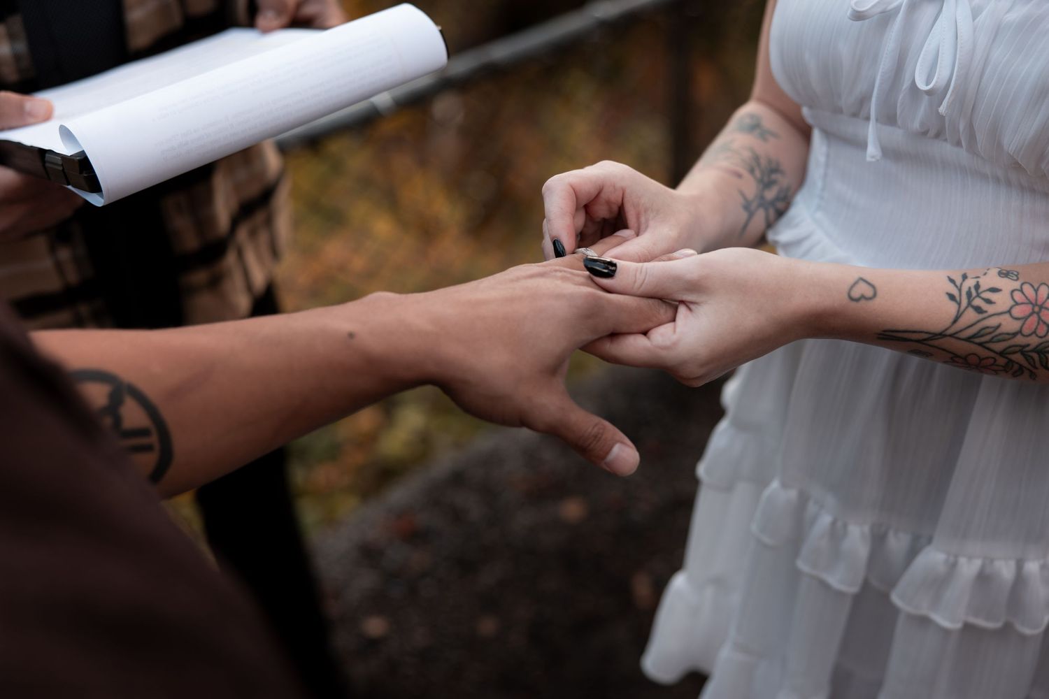 A close-up sequence of hands exchanging wedding rings during an outdoor ceremony.