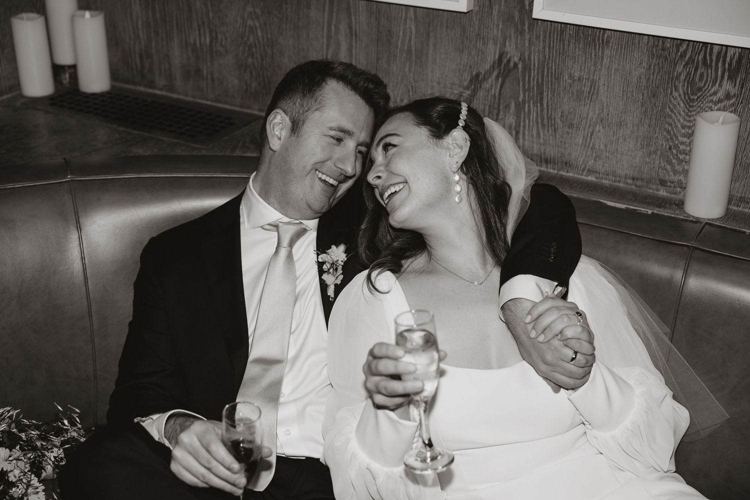 A black and white wedding photo of a couple sharing a joyful moment together in the back of a car.