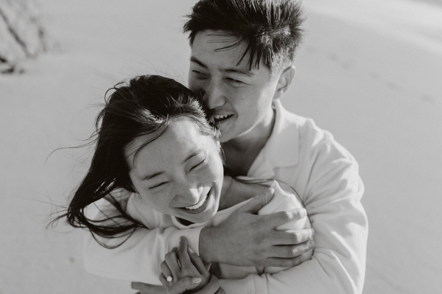Black and white photo of a joyful Asian couple embracing and laughing together on a beach.