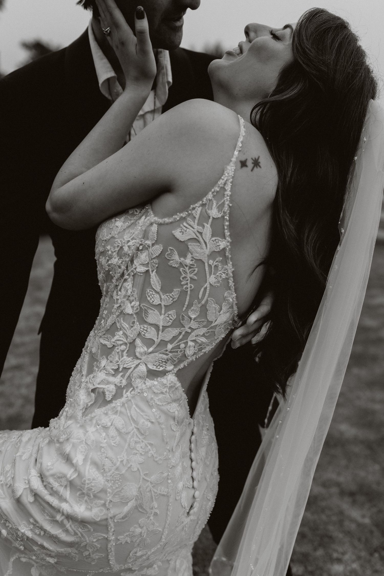 Romantic black and white wedding photo showing bride in lace gown with small tattoo on her back.