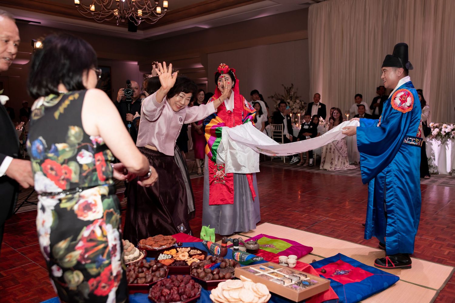 Korean traditional wedding ceremony with guests in hanbok attire dancing and celebrating at a elegant reception venue.