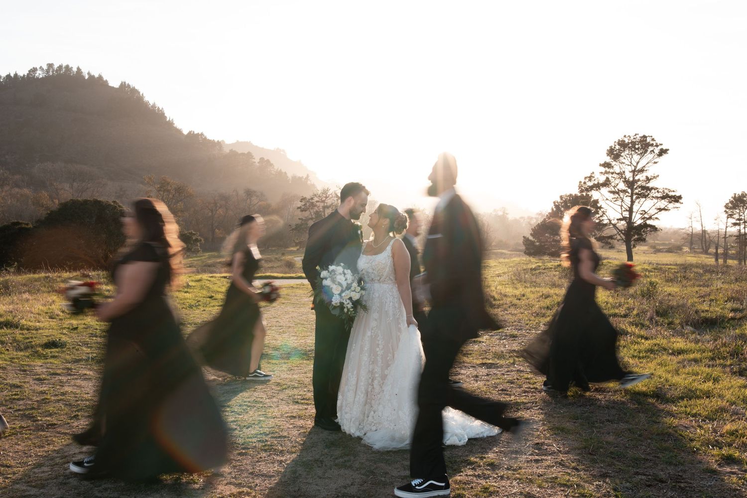 Wedding couple embraces on a hilltop at sunset while photographer captures their special moment.