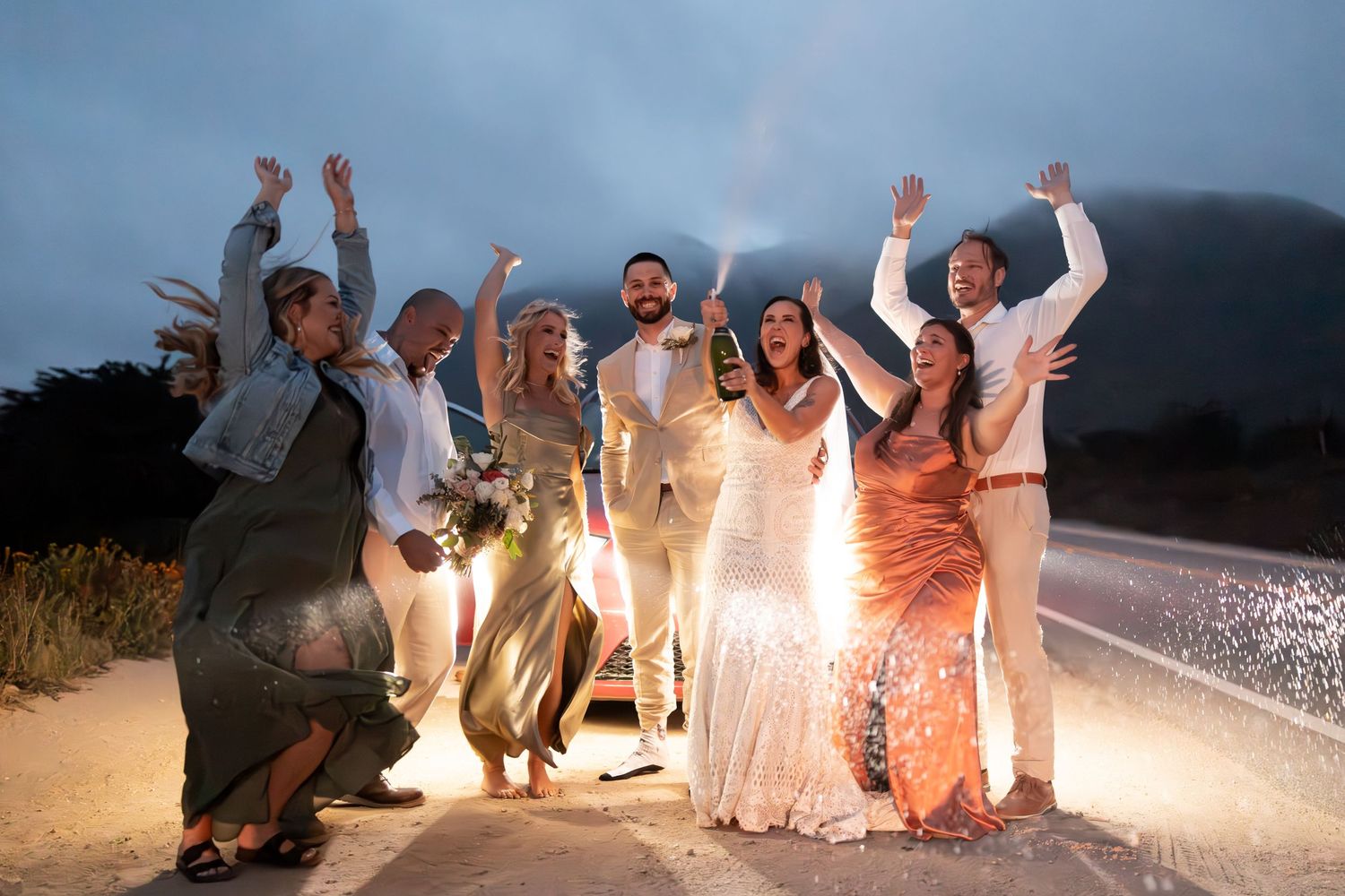 Group of people celebrating at a beach party with sparklers and bonfires at night.