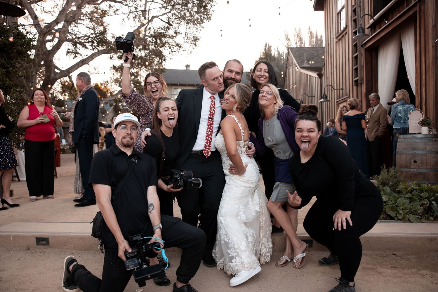 Wedding party poses together outdoors in formal attire with black suits and a white dress.