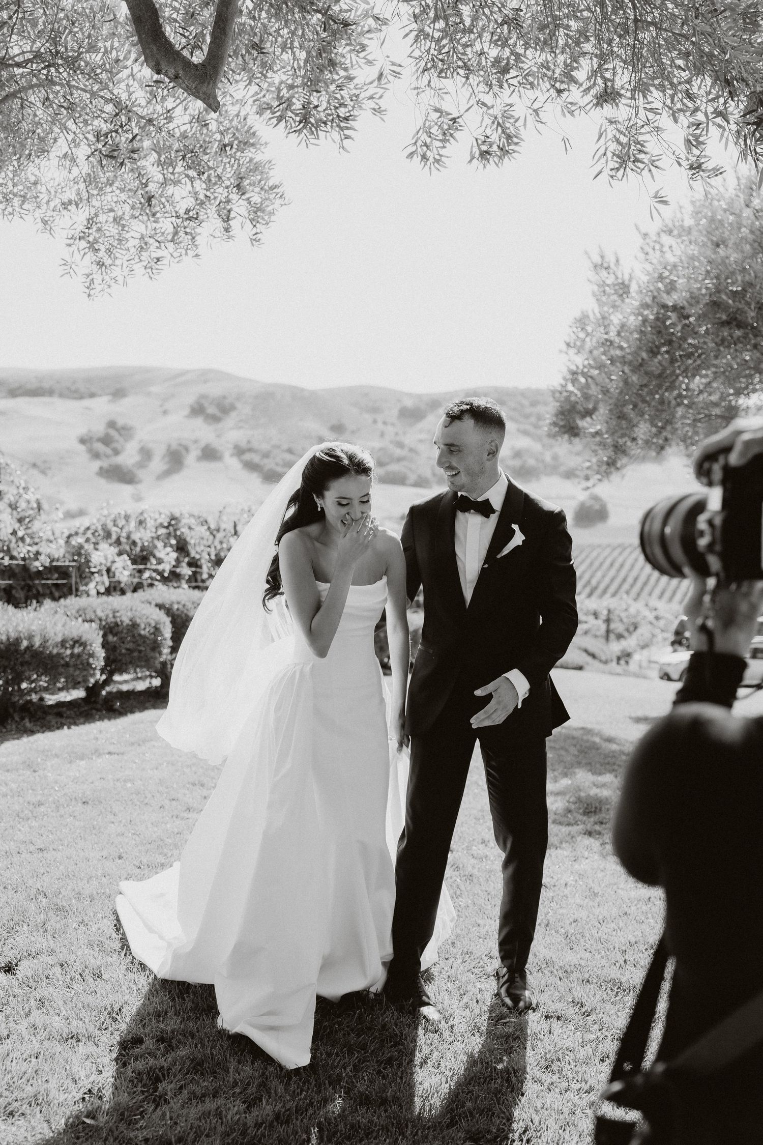 A black and white wedding photo series showing a couple and photographer in an outdoor vineyard setting.