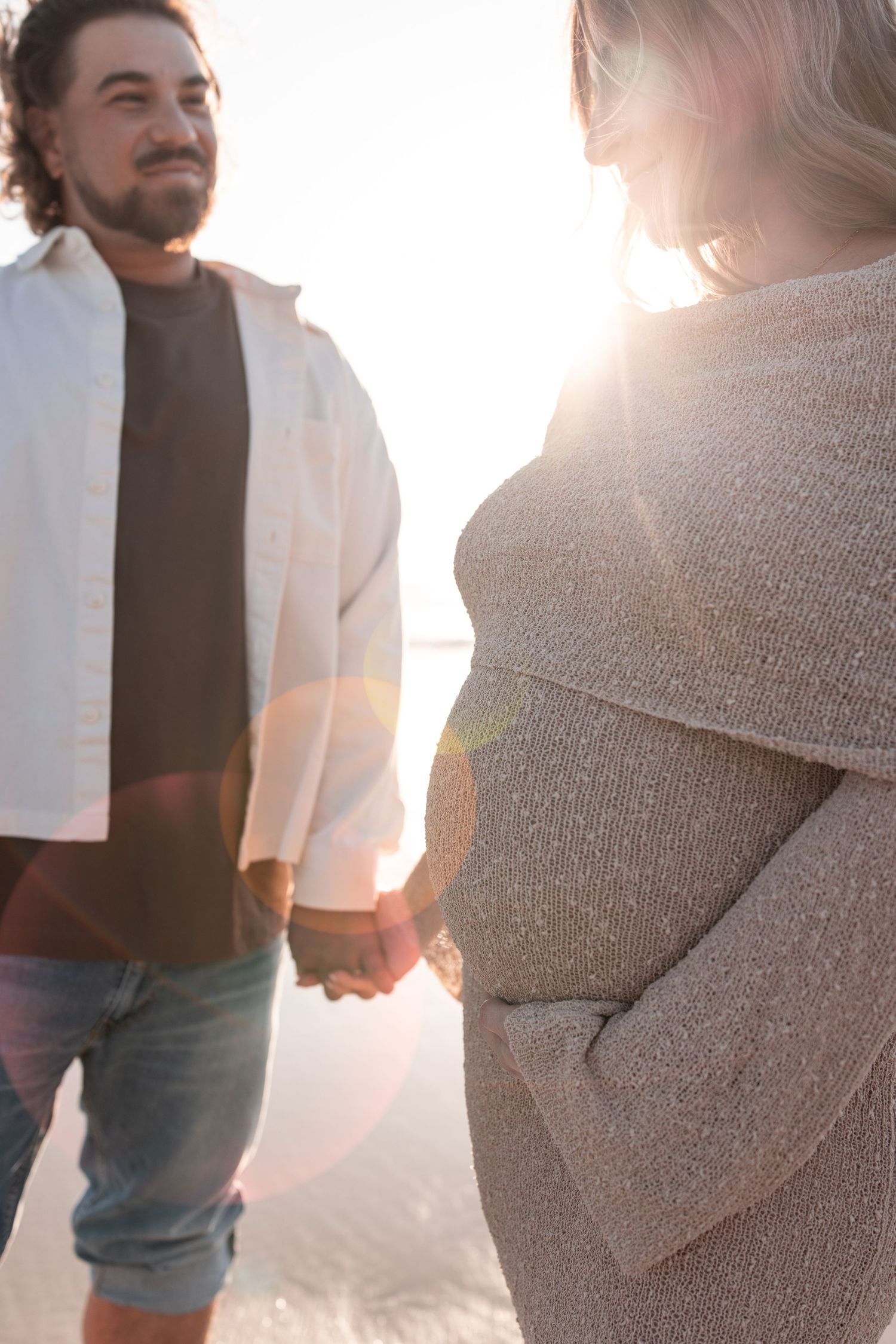 A couple holding hands at sunset with warm backlighting creating a romantic silhouette against a bright sky.