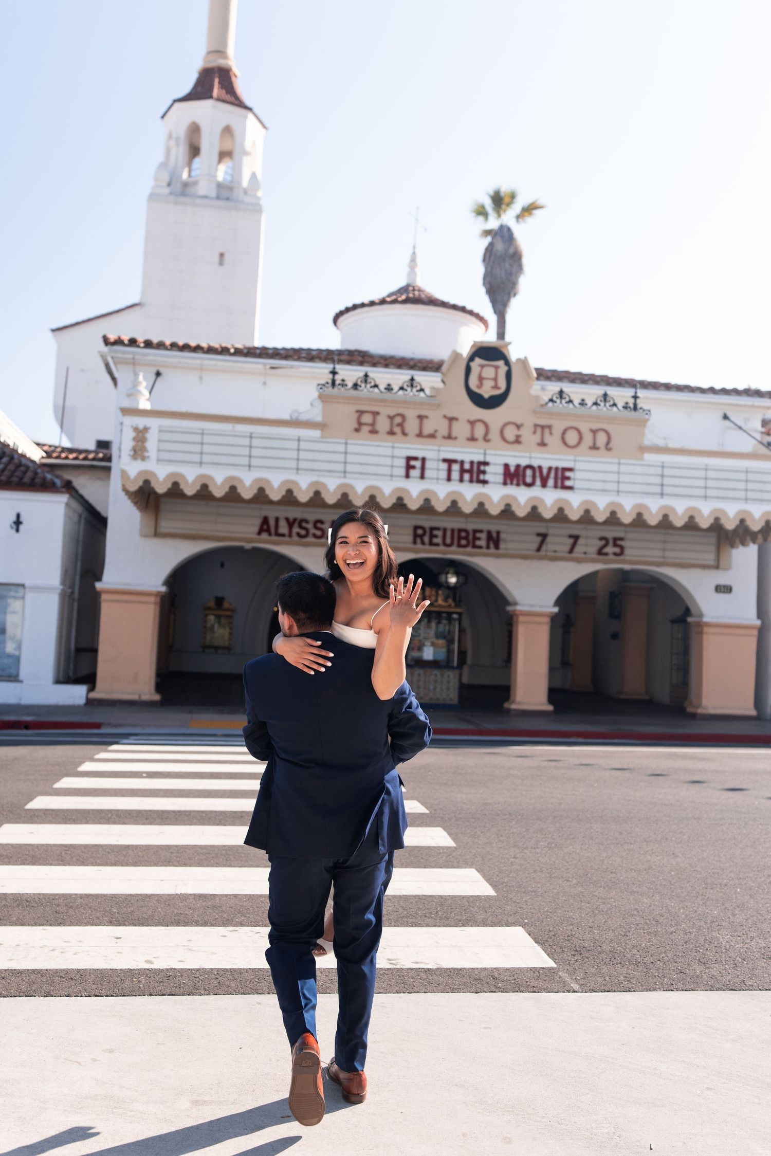 Small child walks across white crosswalk towards historic Spanish-style movie theater entrance.